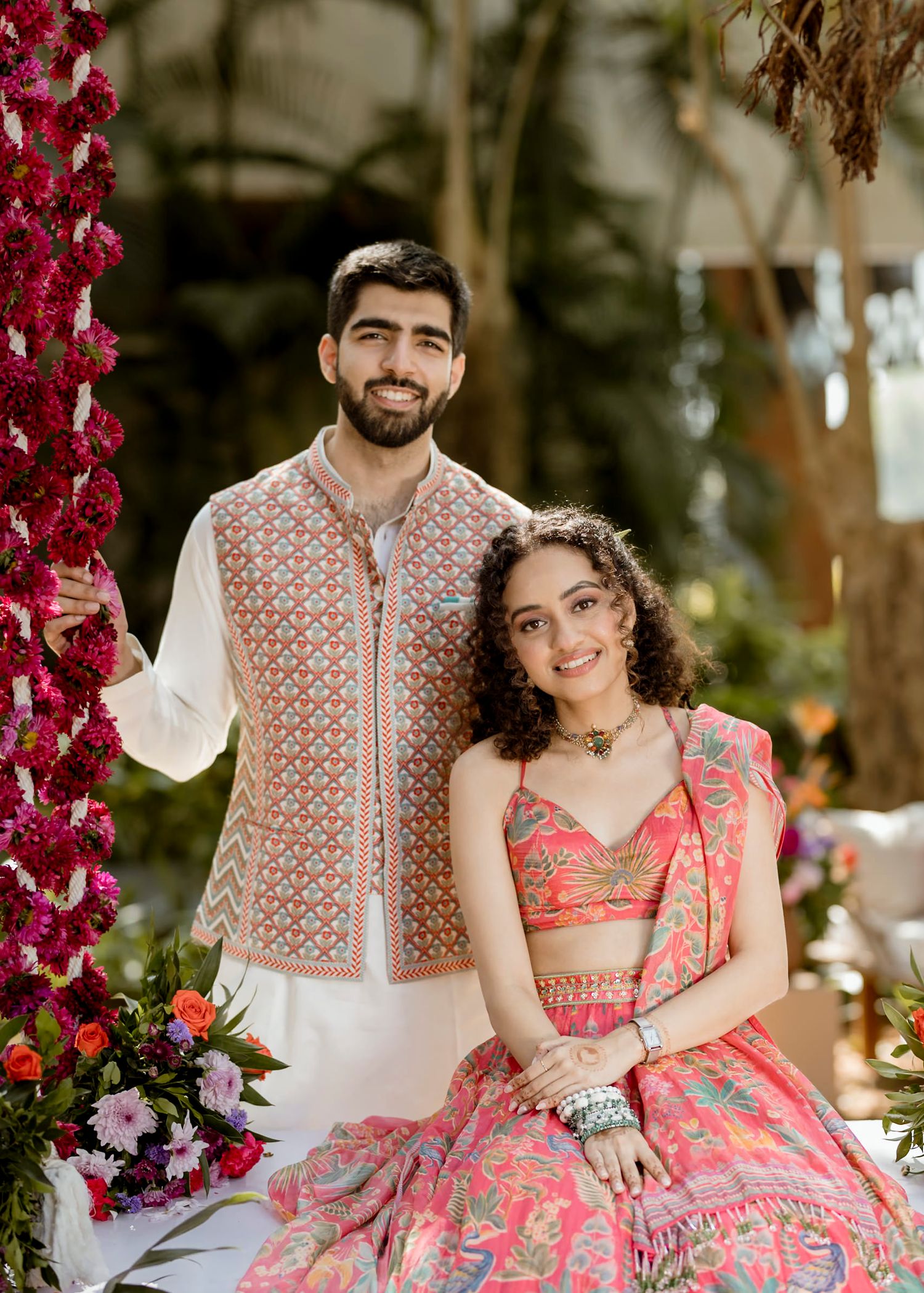 A couple shares intimate moments in coordinated pink and white Indian wedding outfits under floral decor.