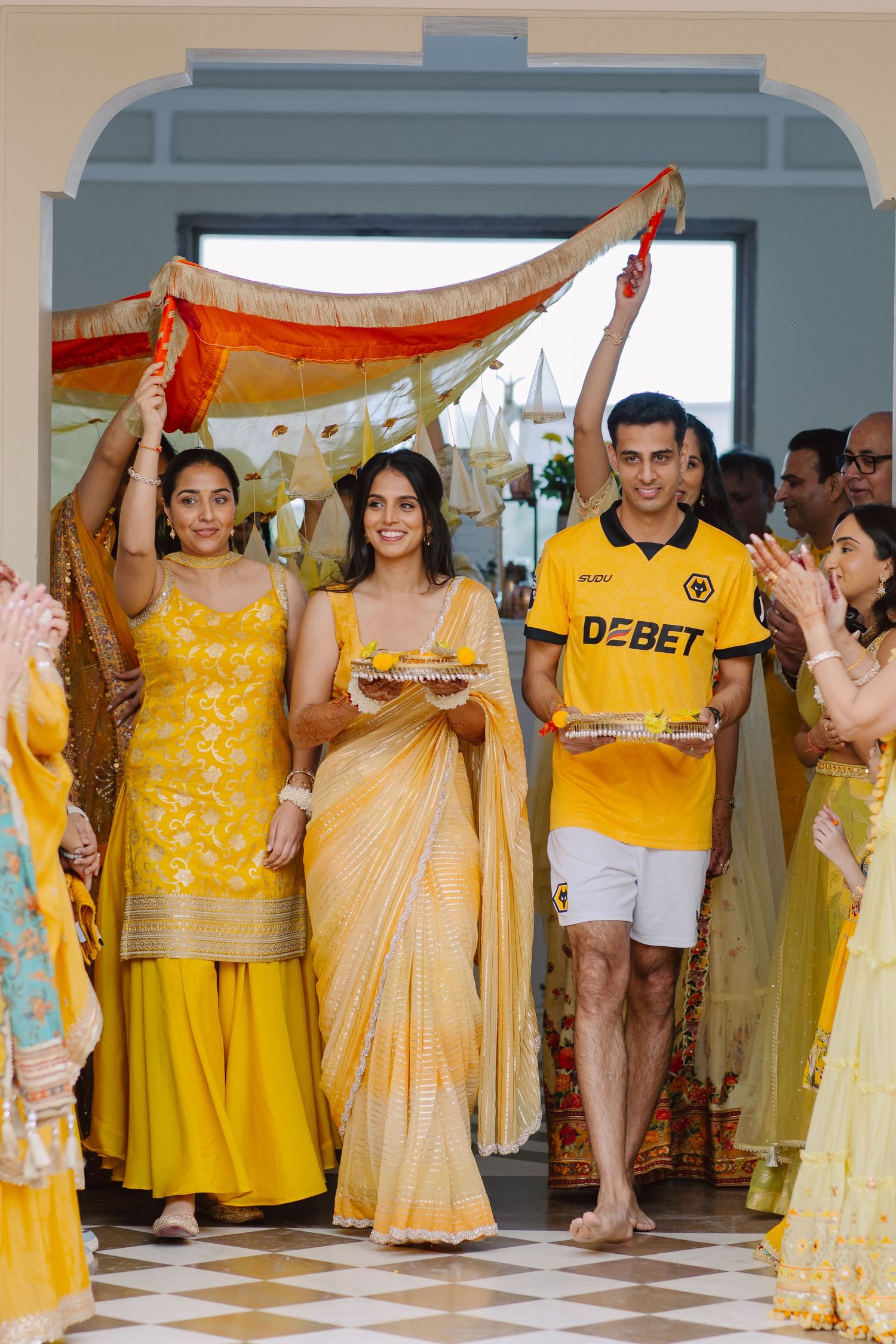 Wedding guests in yellow and gold attire gather during a festive celebration.