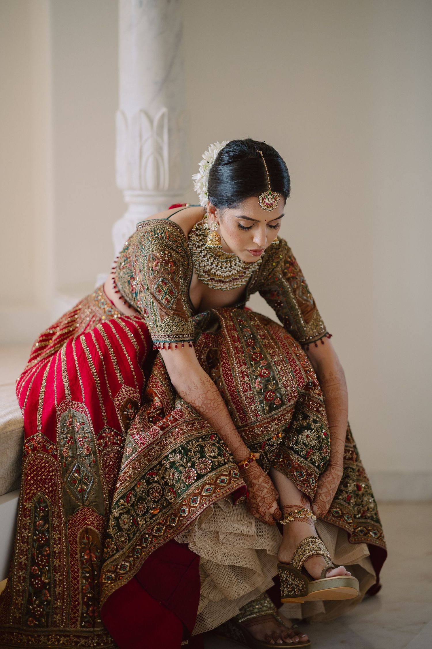 Bride in traditional red and gold lehenga adjusting her footwear.