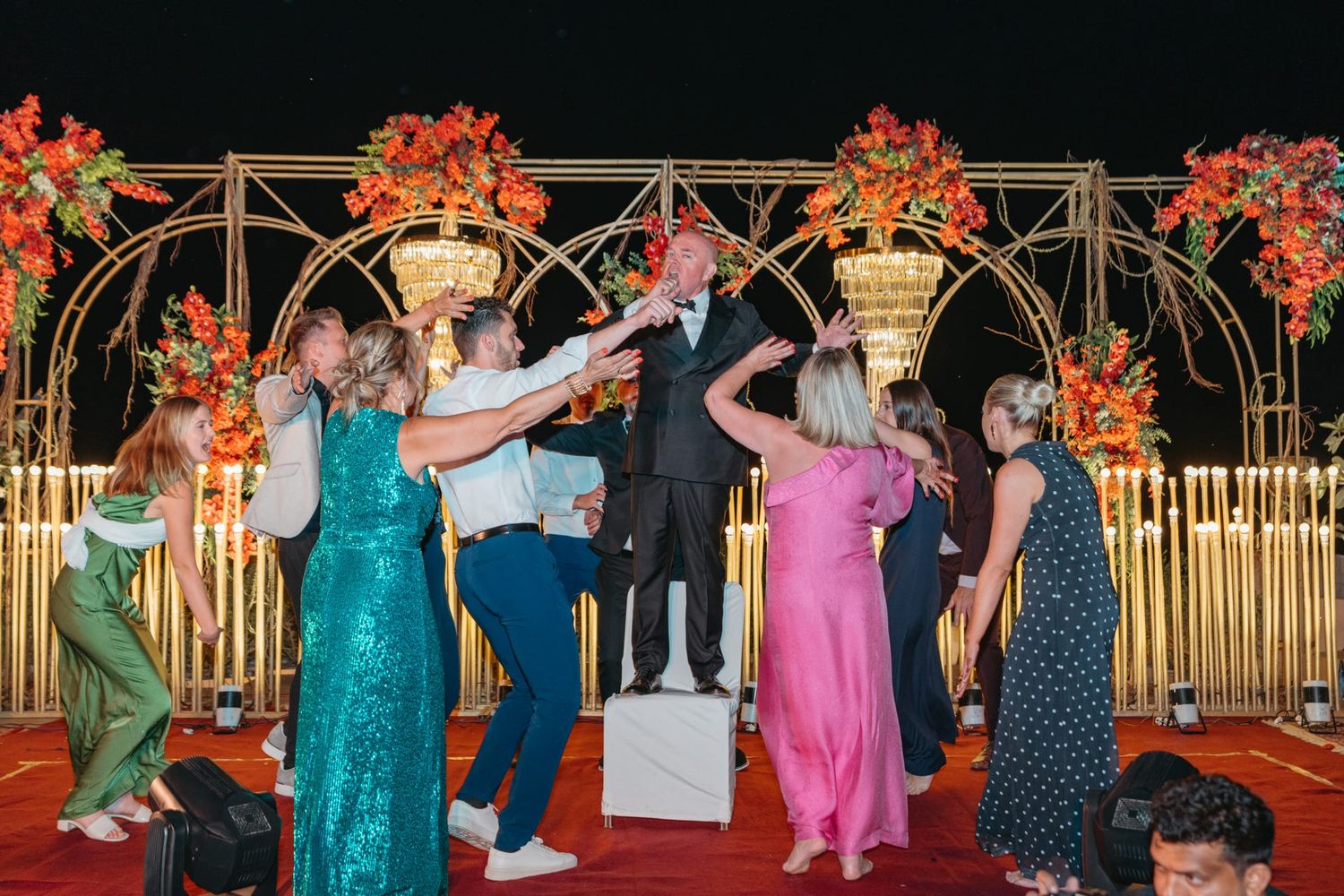 Wedding reception with colorful attire and bamboo backdrop decorated with orange florals.