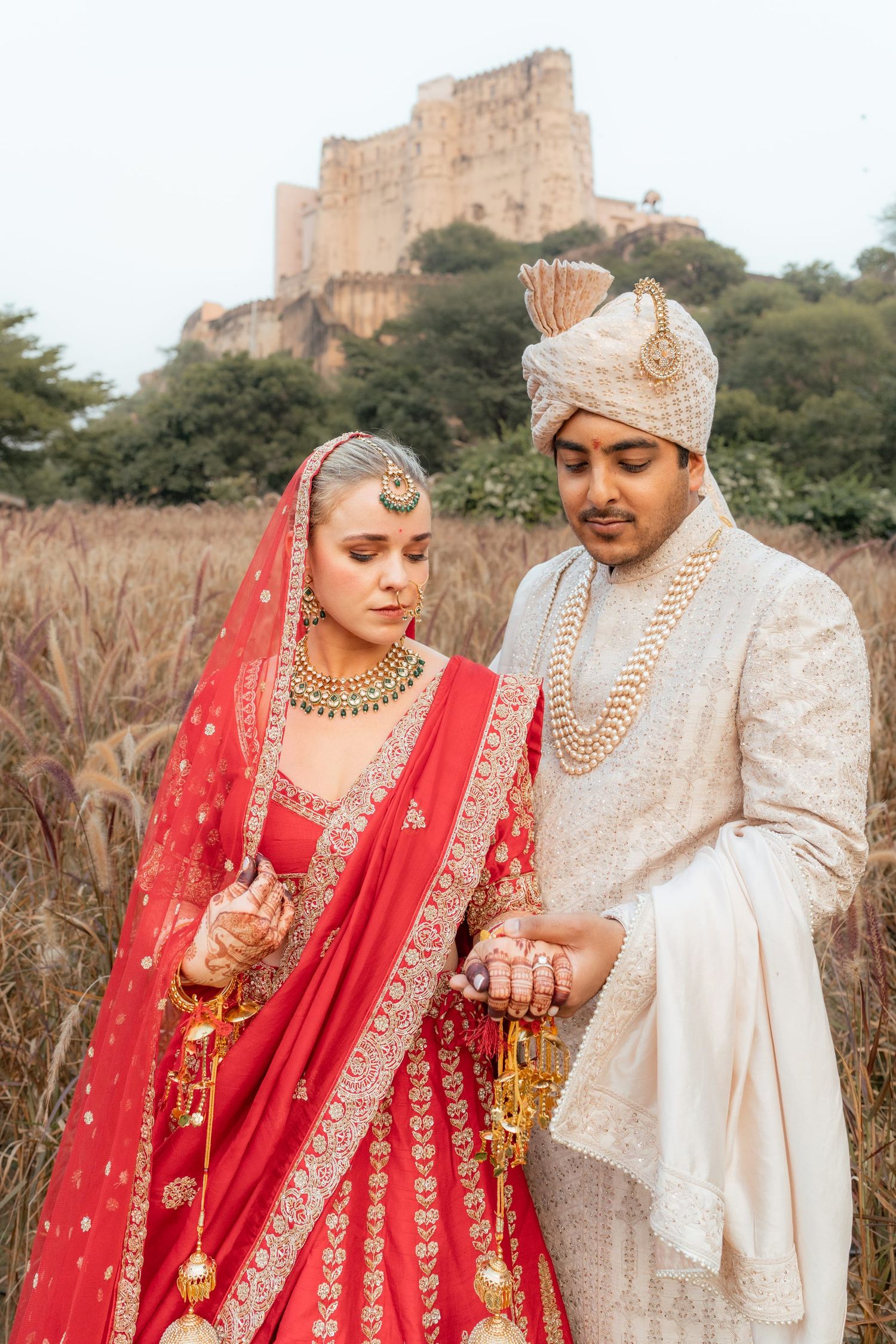 Newlyweds in traditional Indian wedding attire share intimate moments against rustic backdrop.