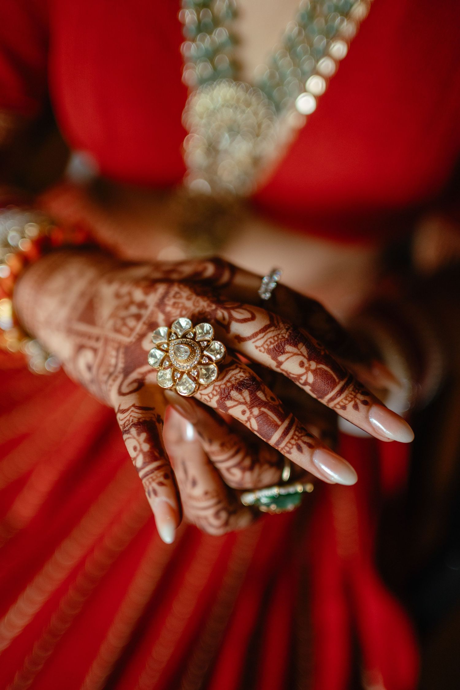 Close-up of bride's hands adorned with intricate henna mehndi, kundan ring, and bangles in traditional Indian bridal red saree.