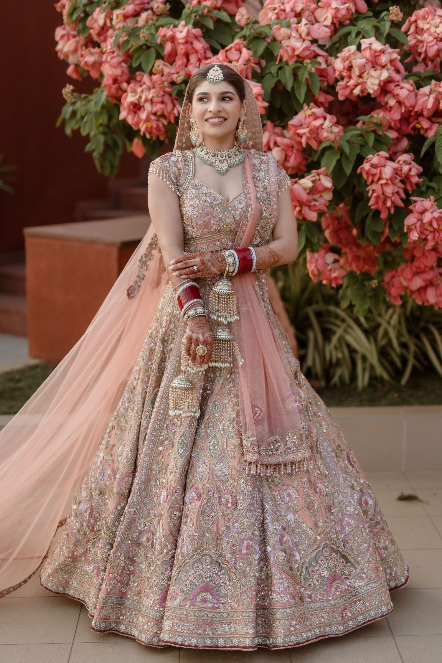 Beautiful peach and silver embroidered bridal lehenga with floral backdrop and traditional Indian wedding attire details.