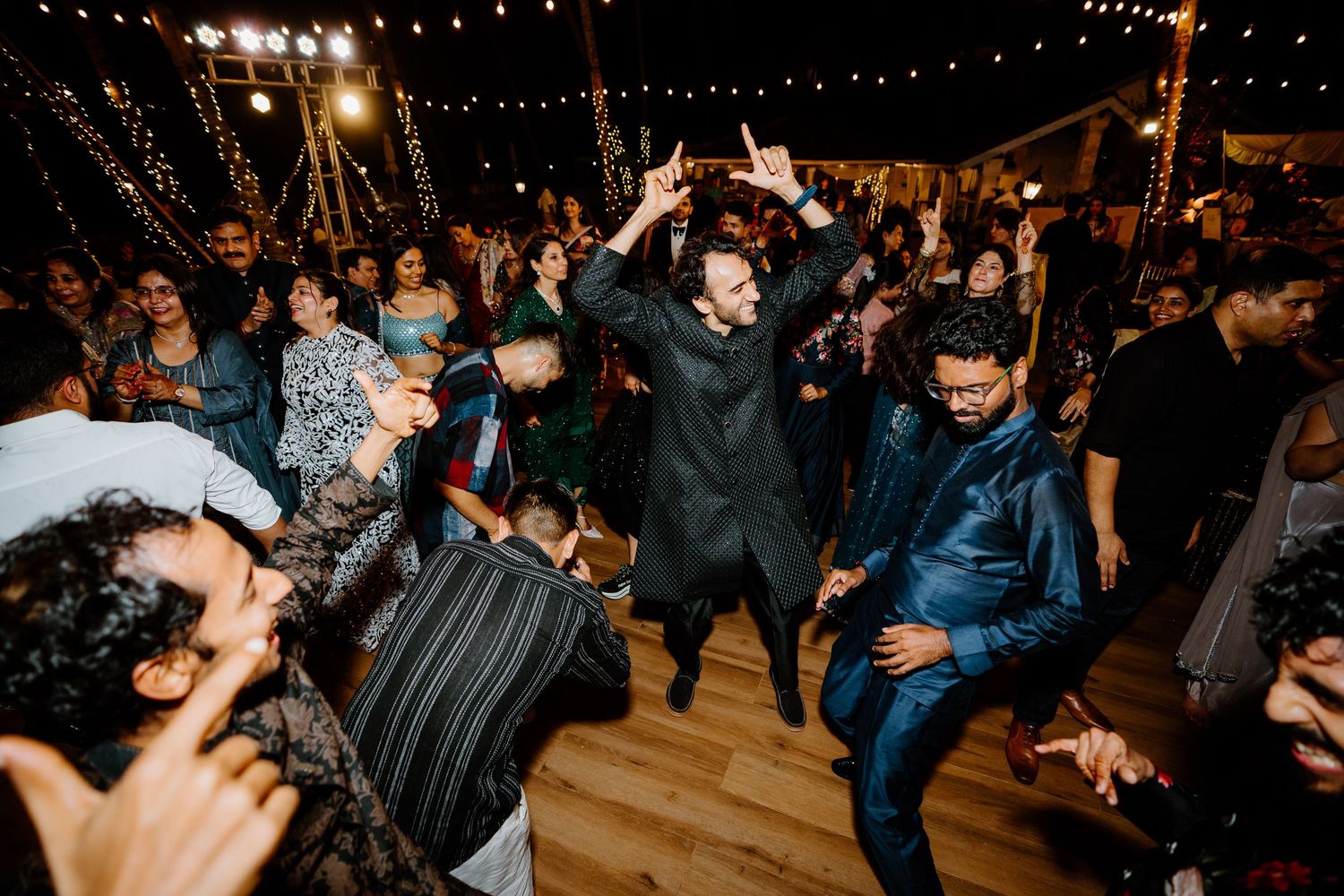 Guests dancing energetically at an outdoor wedding reception under string lights at night.
