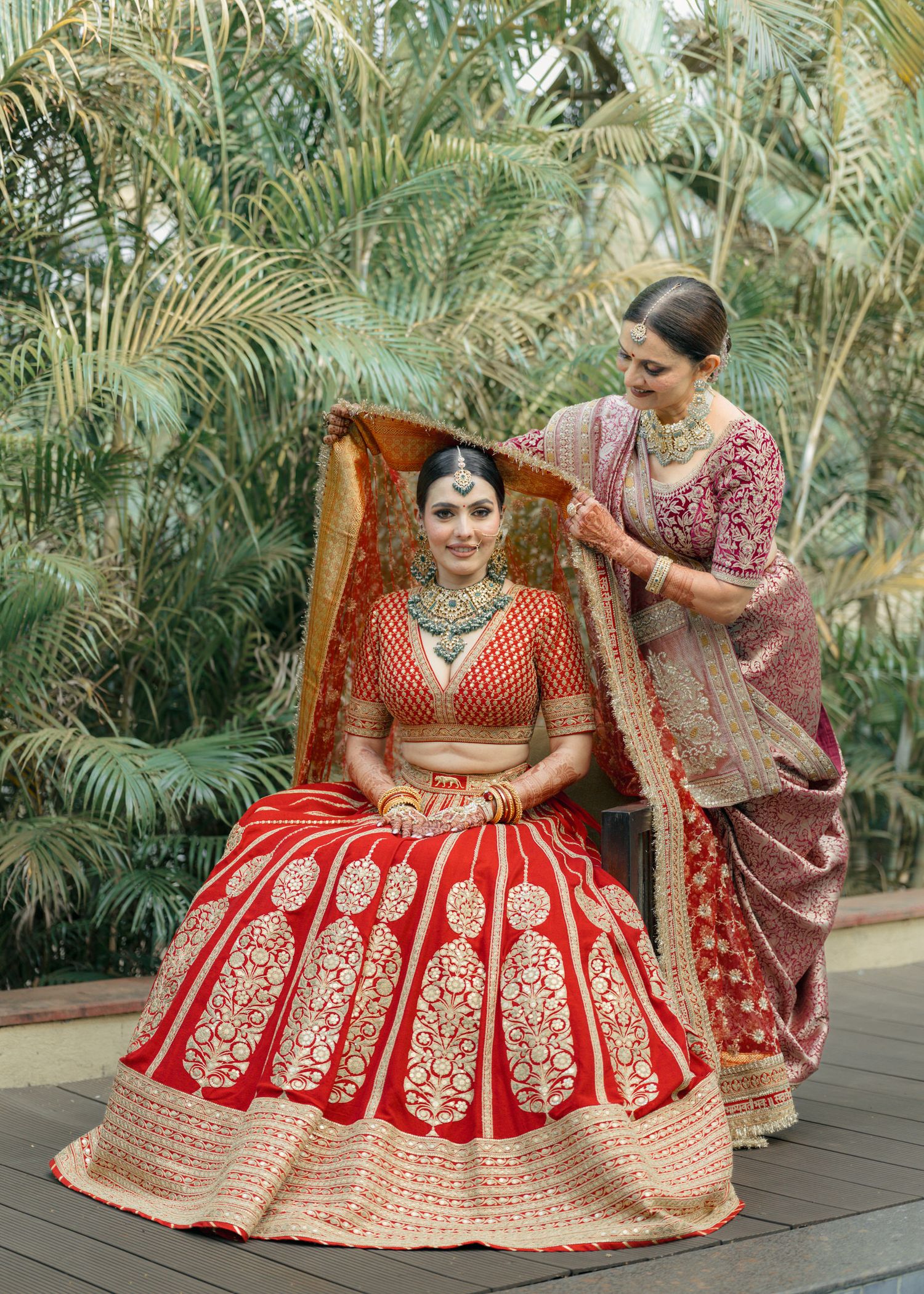 Traditional South Asian bridal attire featuring a red and gold embroidered lehenga with intricate designs in a tropical setting.
