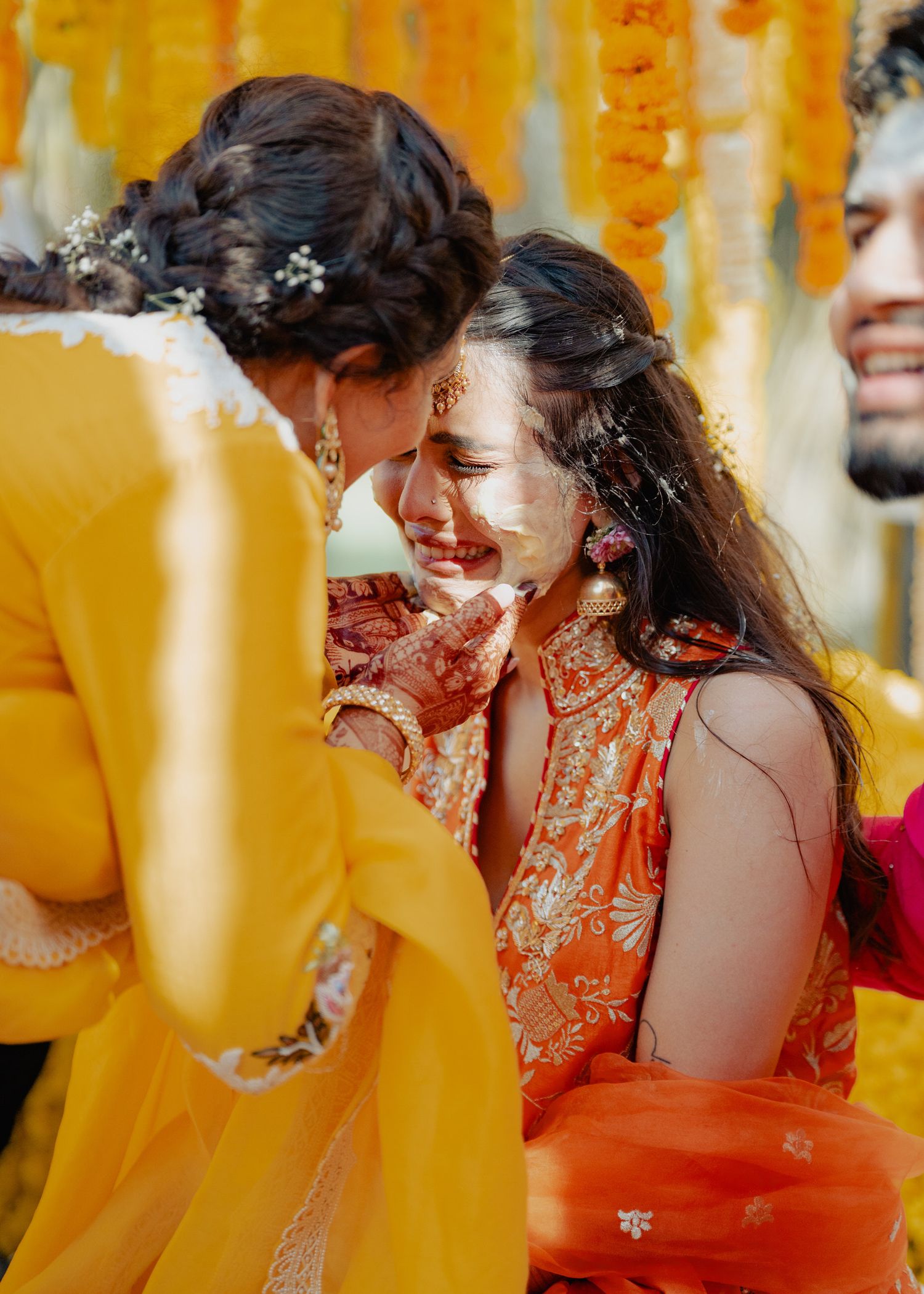 Person dressed in bright orange traditional attire laughs joyfully during a festive celebration ceremony.