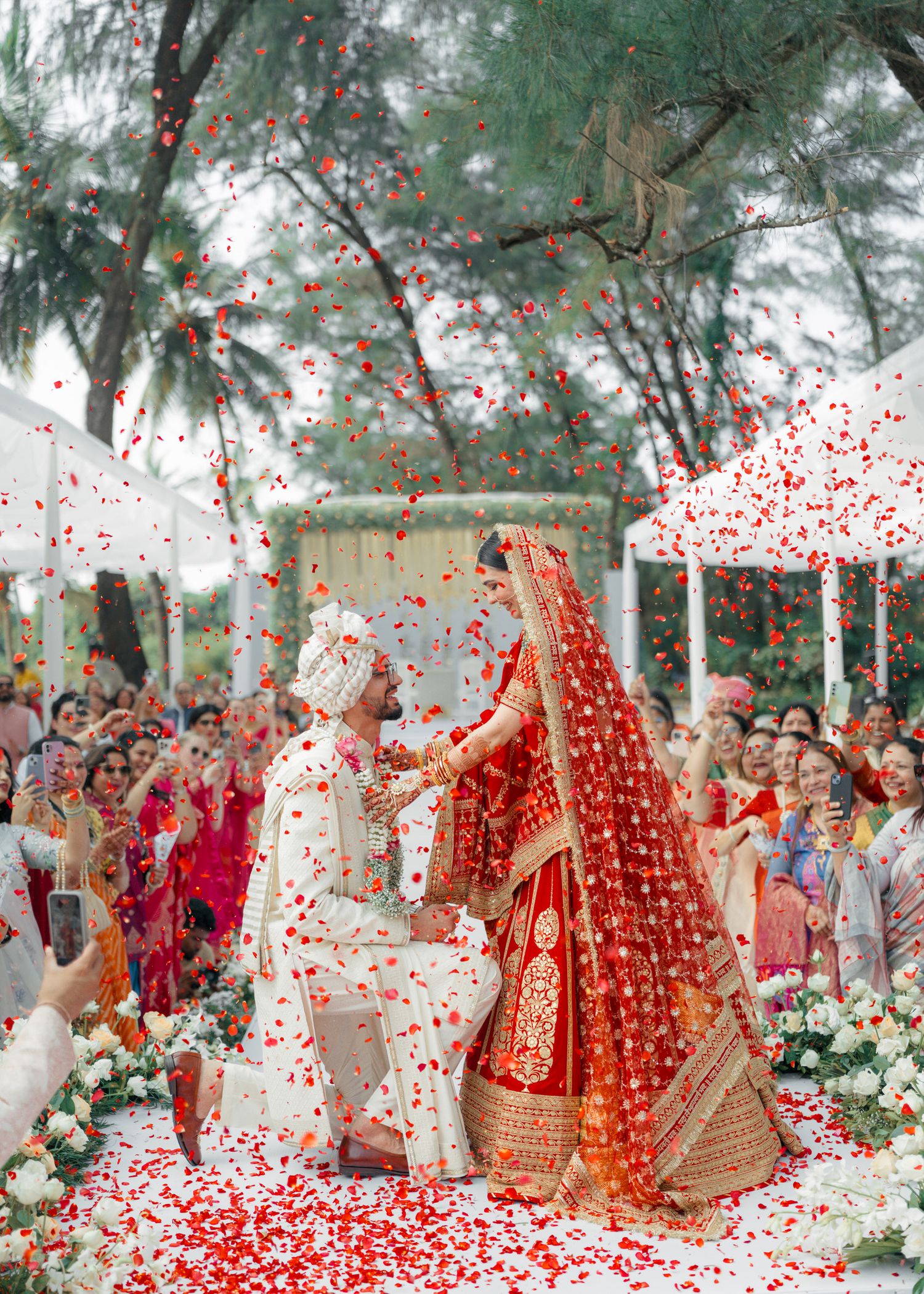 A traditional Indian wedding ceremony with rose petals raining down as couple performs rituals under a floral canopy.
