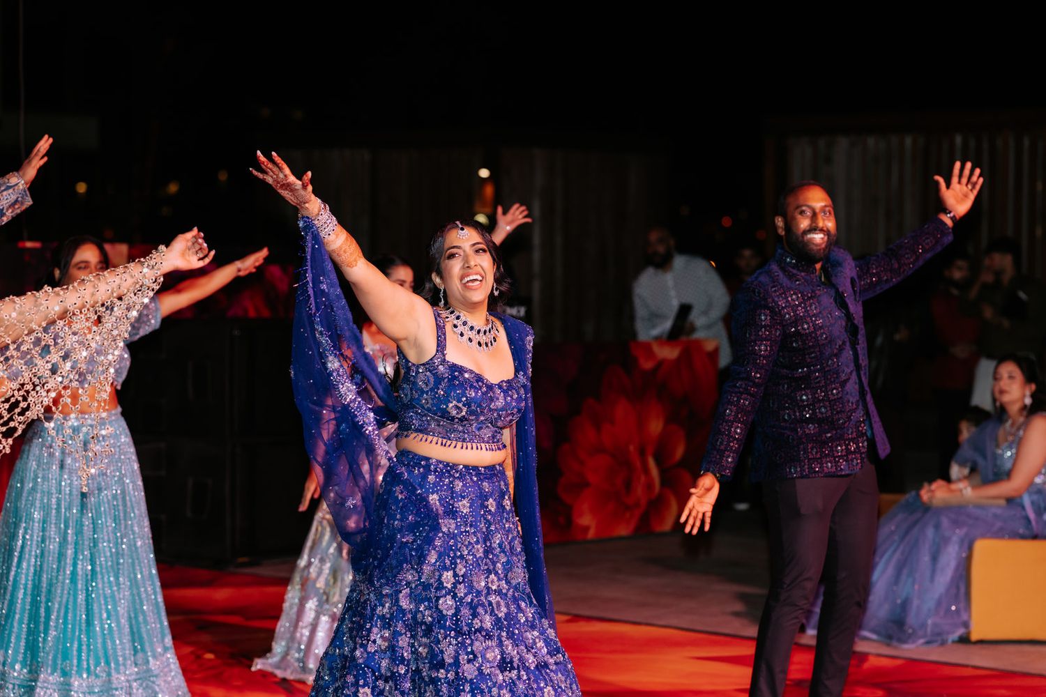 Indian couple in blue traditional attire dancing joyfully at a festive Sangeet celebration.
