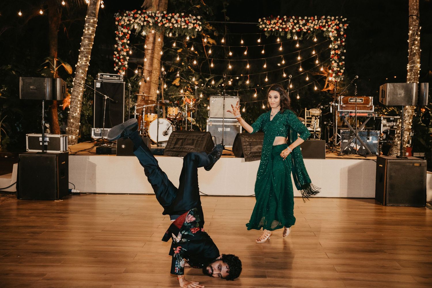 Man breakdancing on dance floor while woman in green dress dances at elegant outdoor wedding reception.