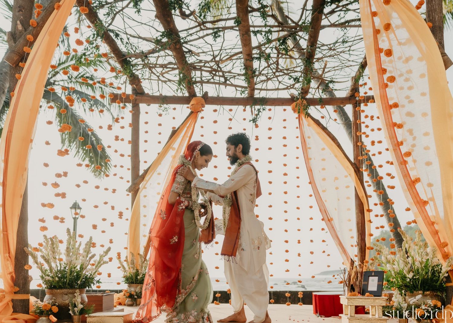 Traditional Indian wedding ceremony under a canopy decorated with orange drapes and fairy lights.