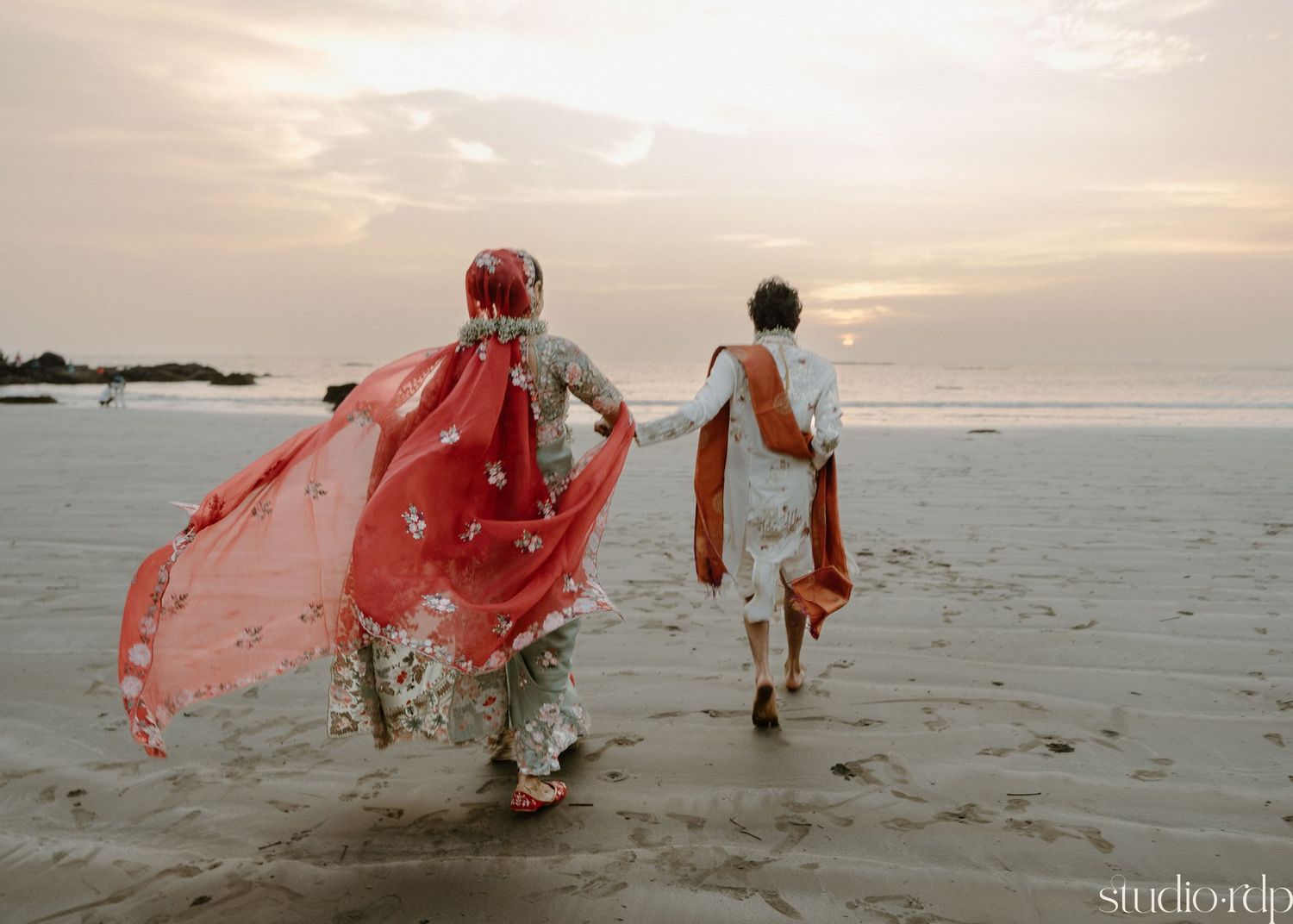 Romantic beach photoshoot at sunset with flowing red fabric in the ocean breeze.