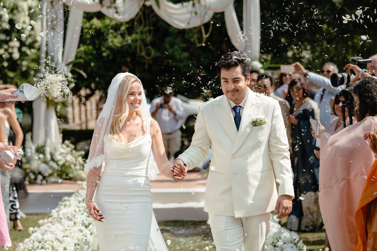 Newlyweds walking together during outdoor garden ceremony with white floral decor.