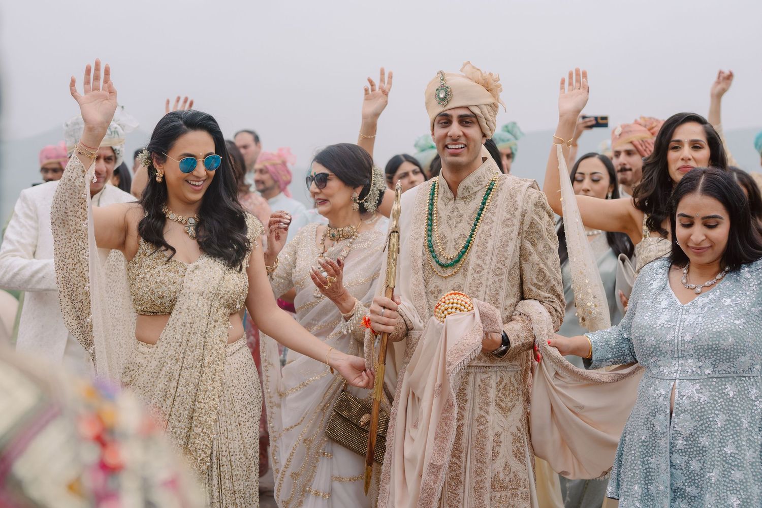Joyful wedding celebration with guests in traditional attire raising hands.