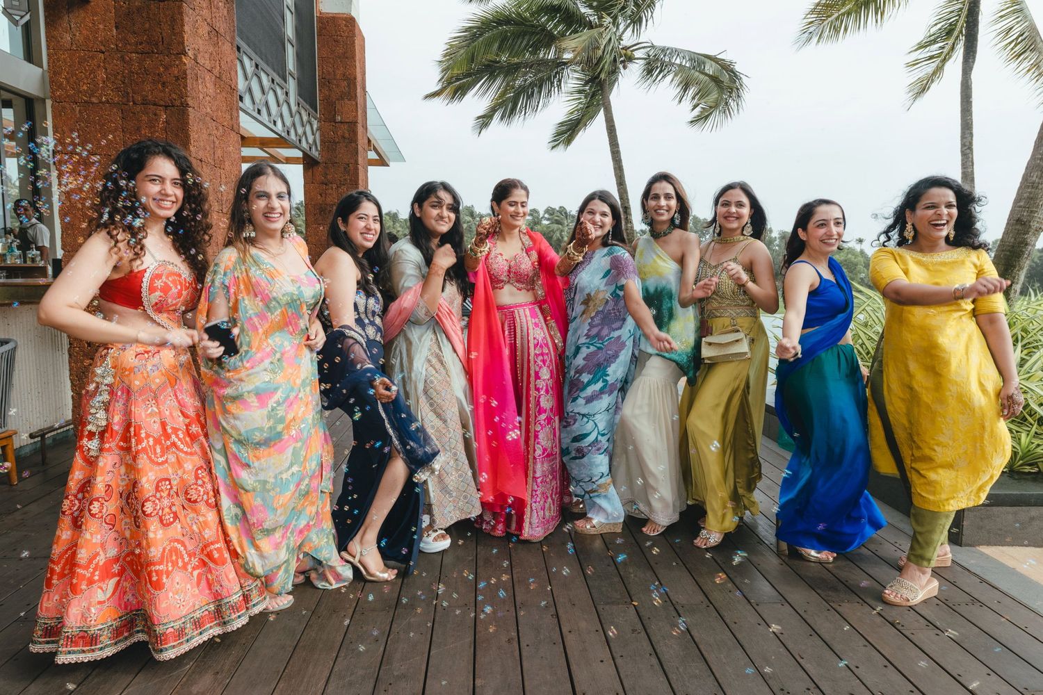 Group of women in colorful traditional Indian attire posing together outdoors at a tropical venue.
