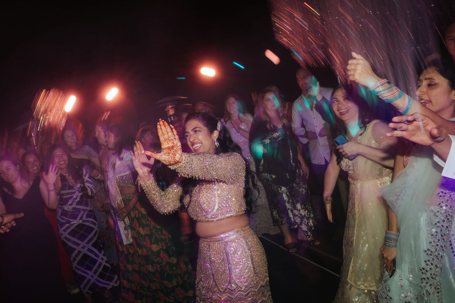 Energetic Indian wedding guests dancing with sparklers on crowded dance floor during festive reception celebration.