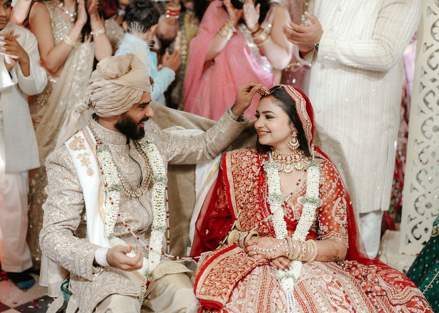 Groom placing sindoor on bride during traditional Indian wedding ceremony while both smile joyfully.