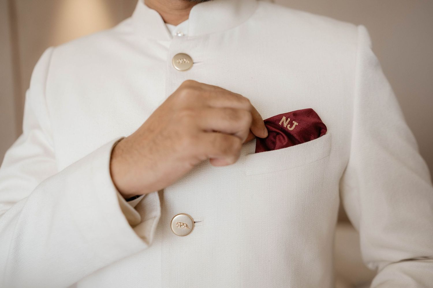 Close up of hands adjusting a burgundy pocket square in the chest pocket of a crisp white formal suit jacket.