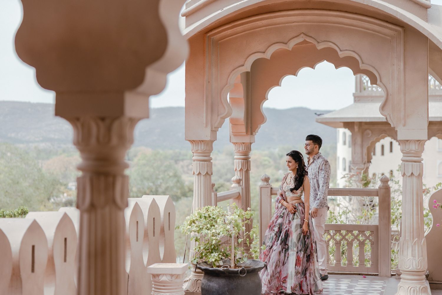 A couple takes romantic photos at a luxurious palace balcony with ornate white stone architecture in India.