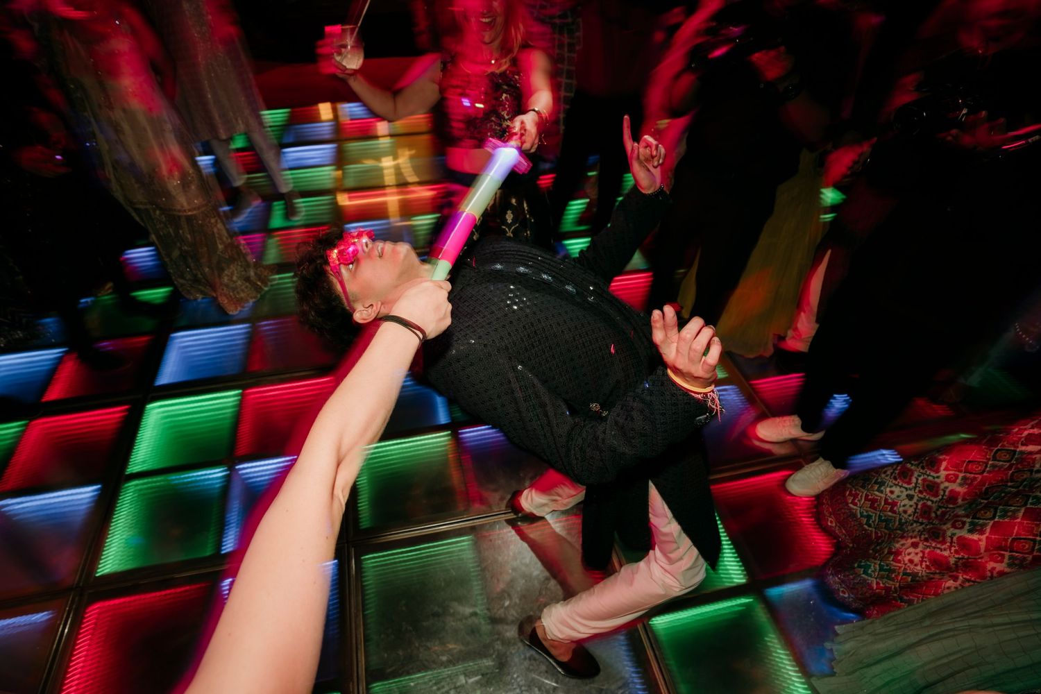 Person dancing on illuminated multicolored dance floor in nightclub with red and green lighting.