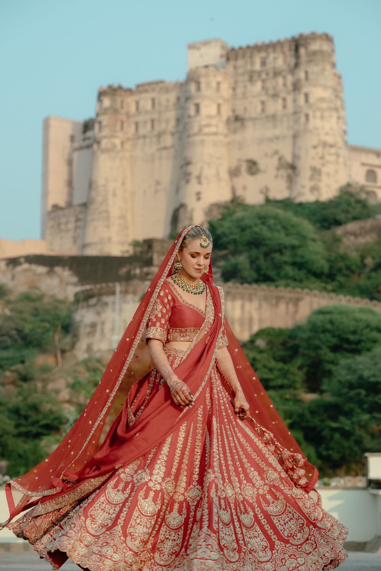 Red bridal lehenga with gold embroidery photographed against historic fort backdrop.
