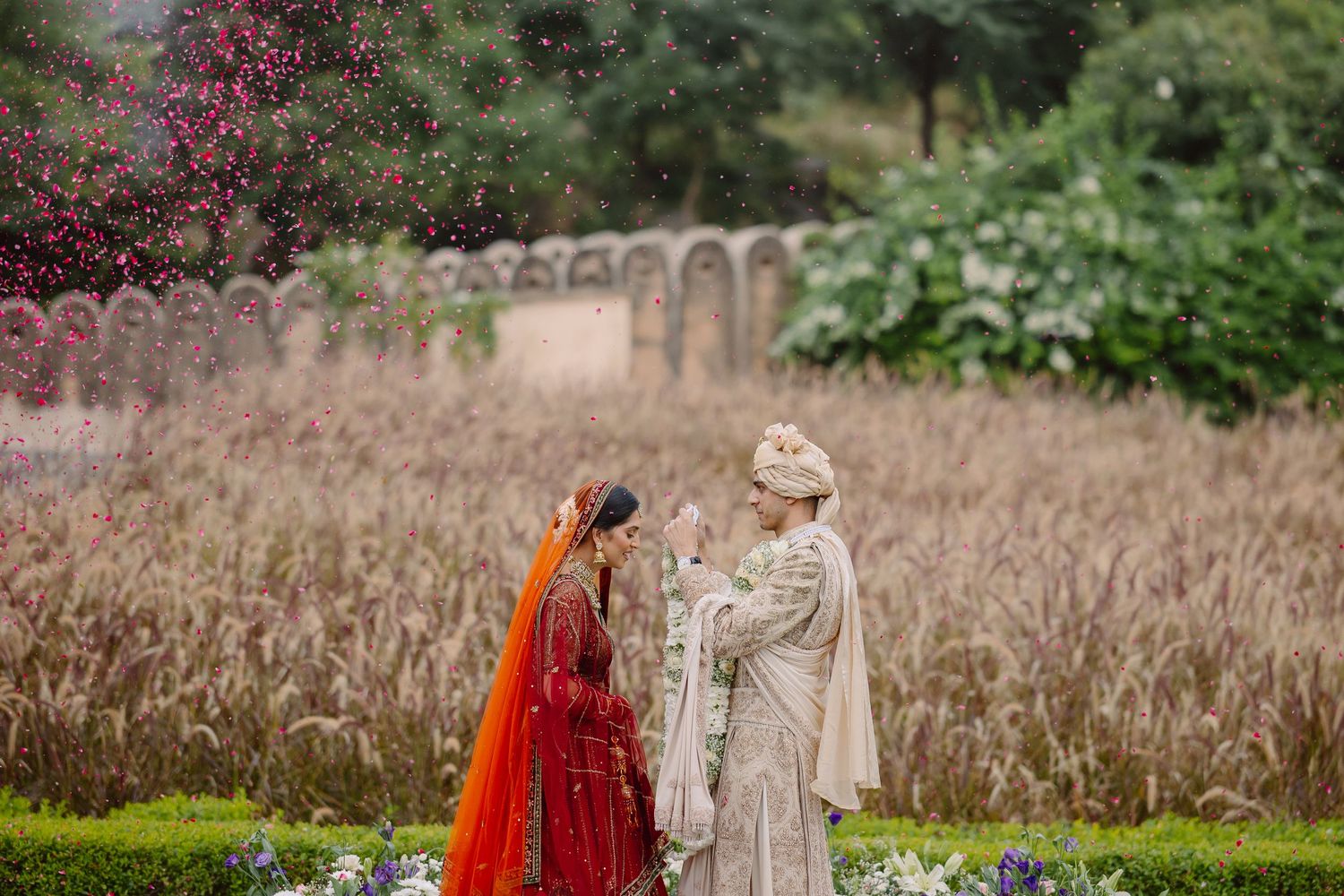 Wedding couple in traditional Indian attire pose in field with floral decorations.