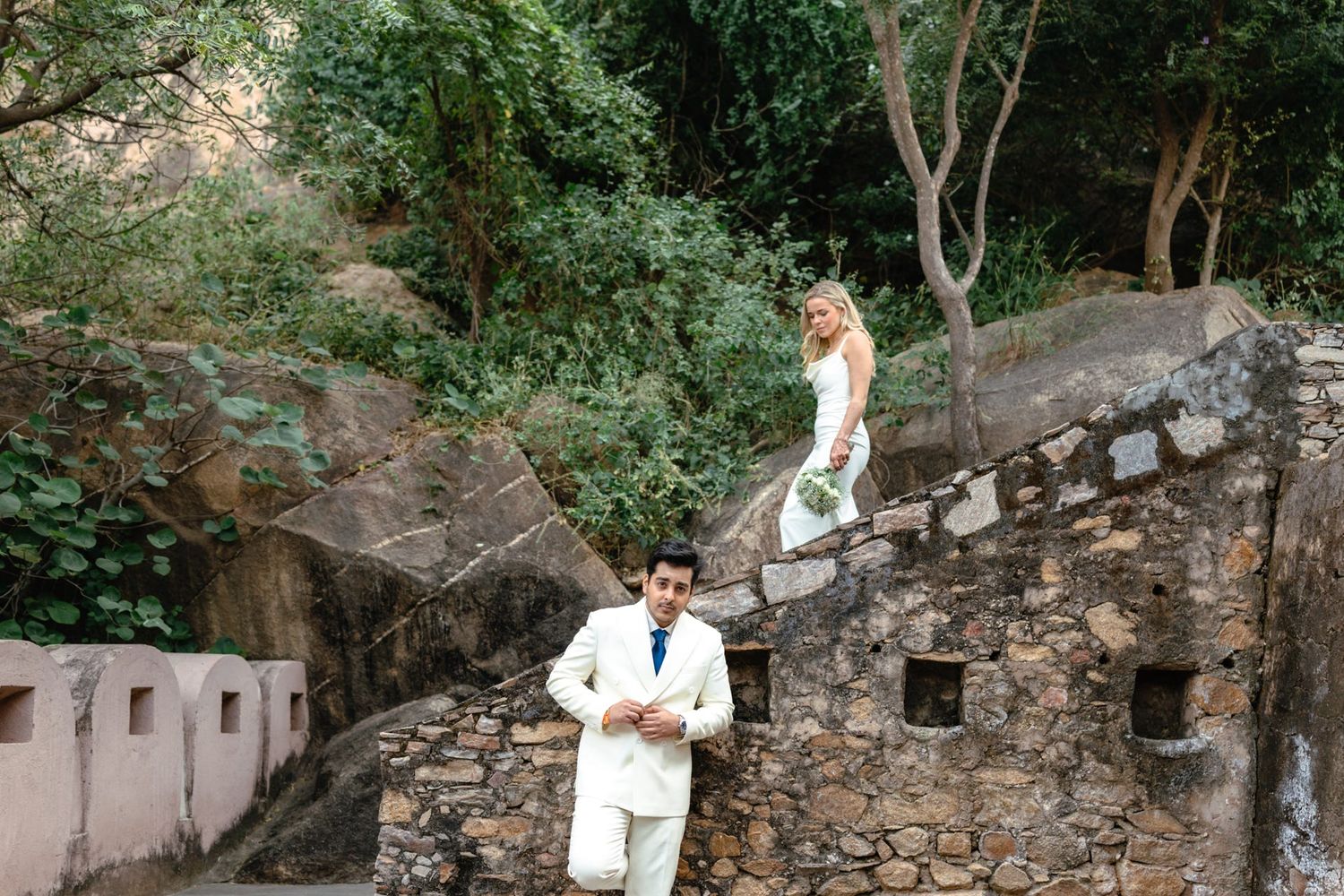 Newlyweds walking through a rustic stone garden path surrounded by lush greenery.