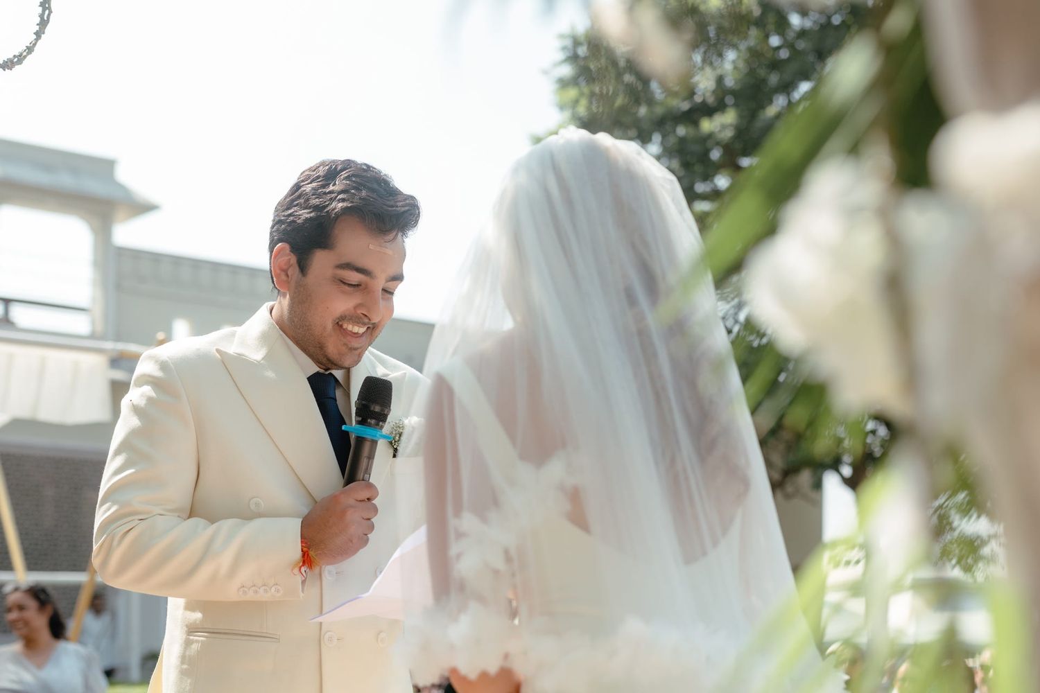 Wedding ceremony moment captured through white drapes and floral decorations outdoors.