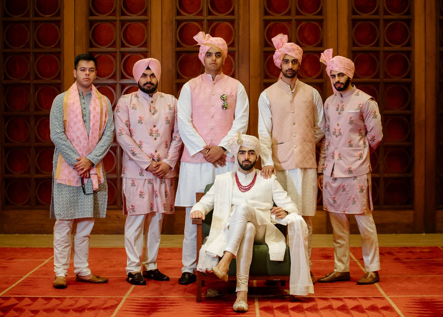 Wedding party members wearing coordinated pink and white formal attire on a red carpet.