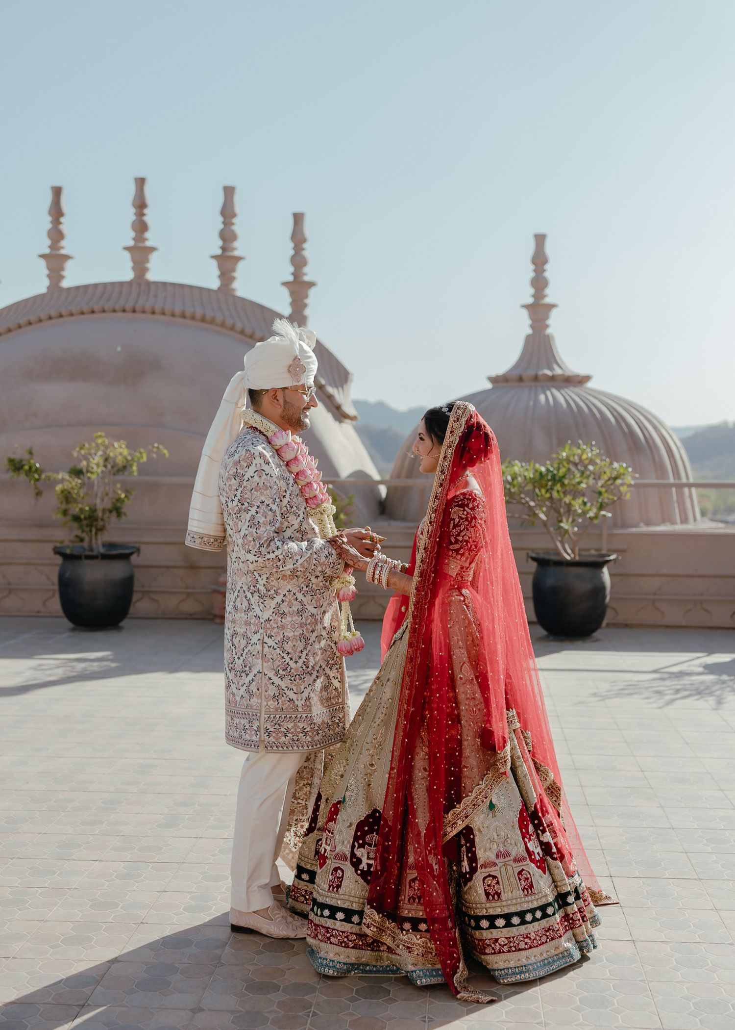Traditional Indian wedding ceremony with couple in ornate attire against domed architecture.