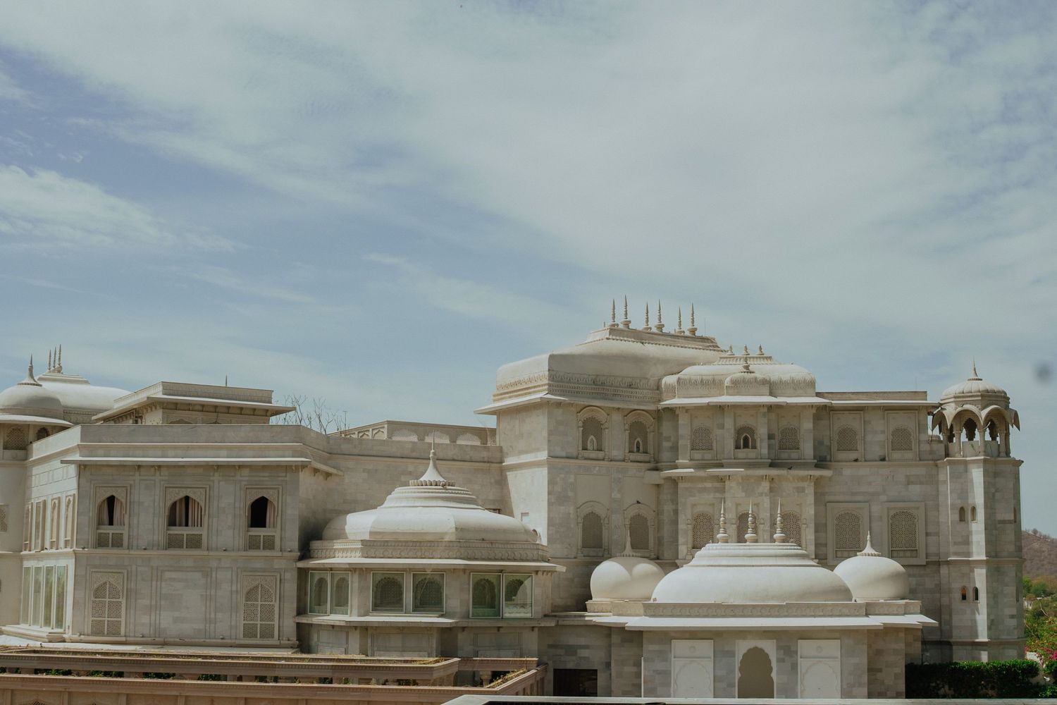 Majestic white marble palace with domed roofs and ornate architecture under cloudy sky in Rajasthan, India.