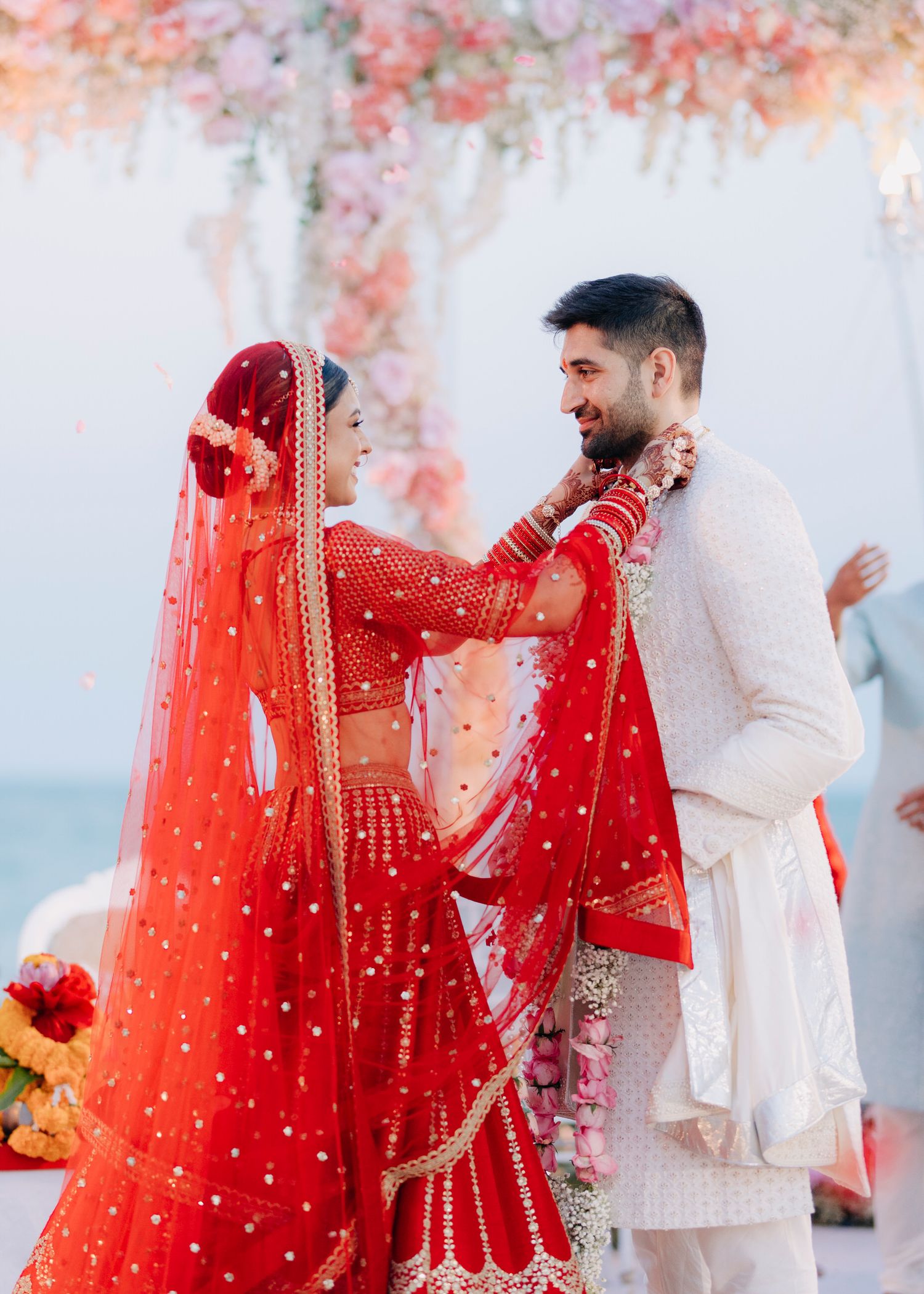 A couple in traditional Indian wedding attire shares romantic moments during their ceremony, with the bride in a stunning red lehenga.