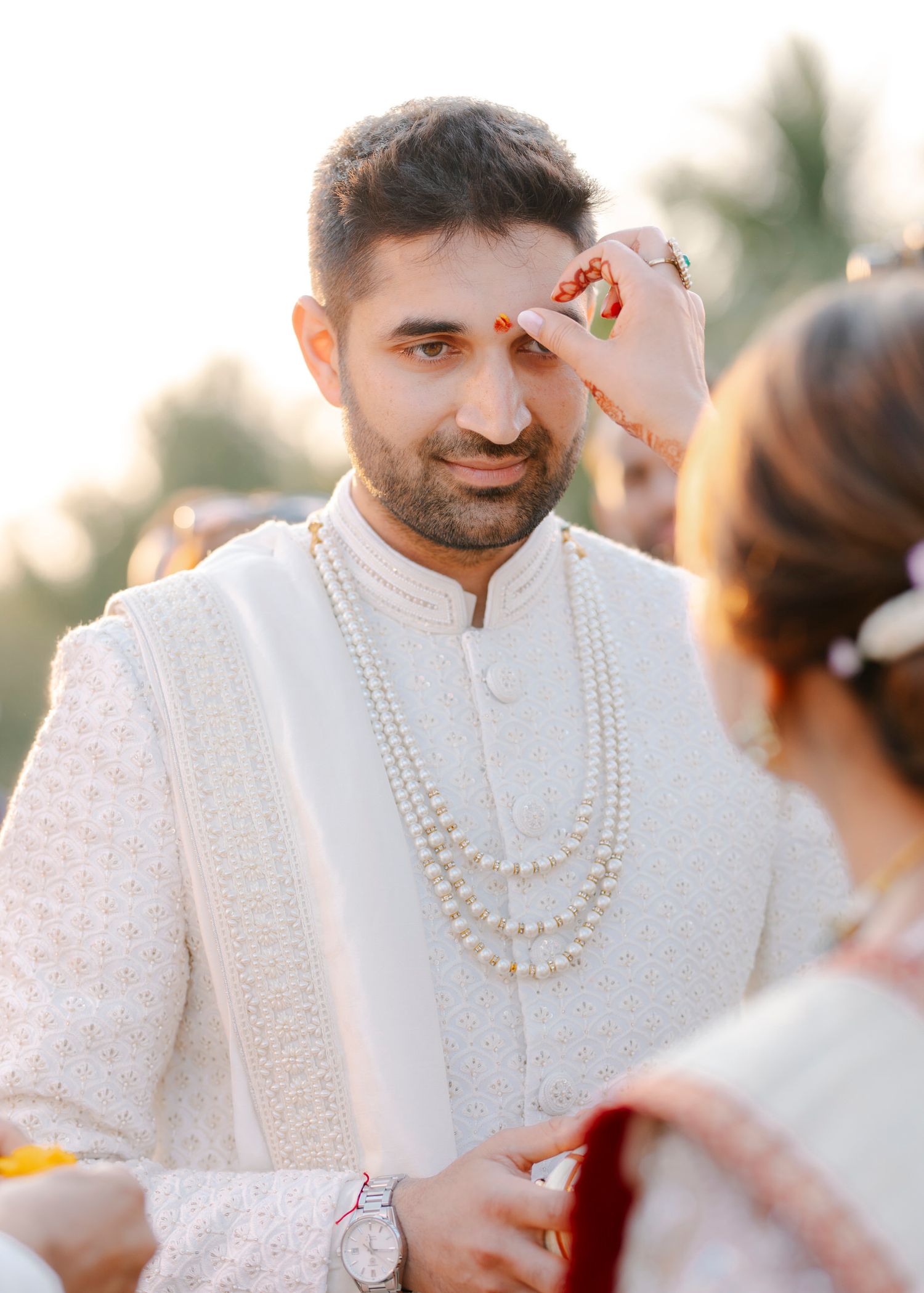 Traditional Indian wedding ceremony showing a groom in white sherwani with pearl necklaces during the sindoor ritual.
