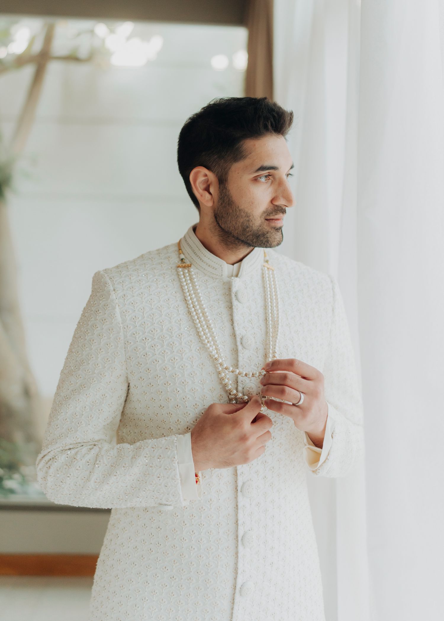 A side view of someone wearing a textured white traditional Indian sherwani suit in an elegant indoor setting.