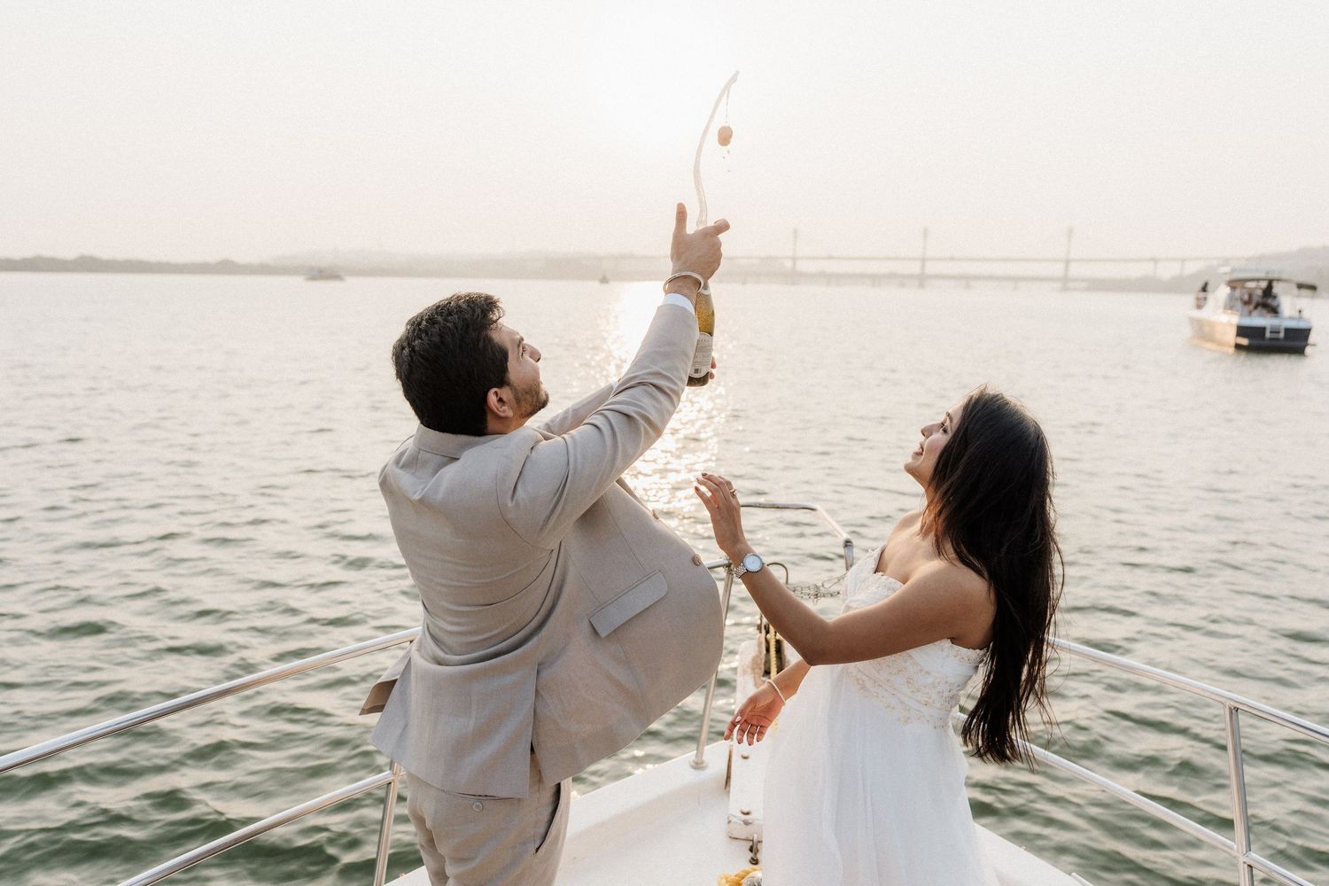 Couple in coordinated white outfits celebrating with champagne on a boat during a sunset pre wedding shoot, captured by Studio RDP Goa