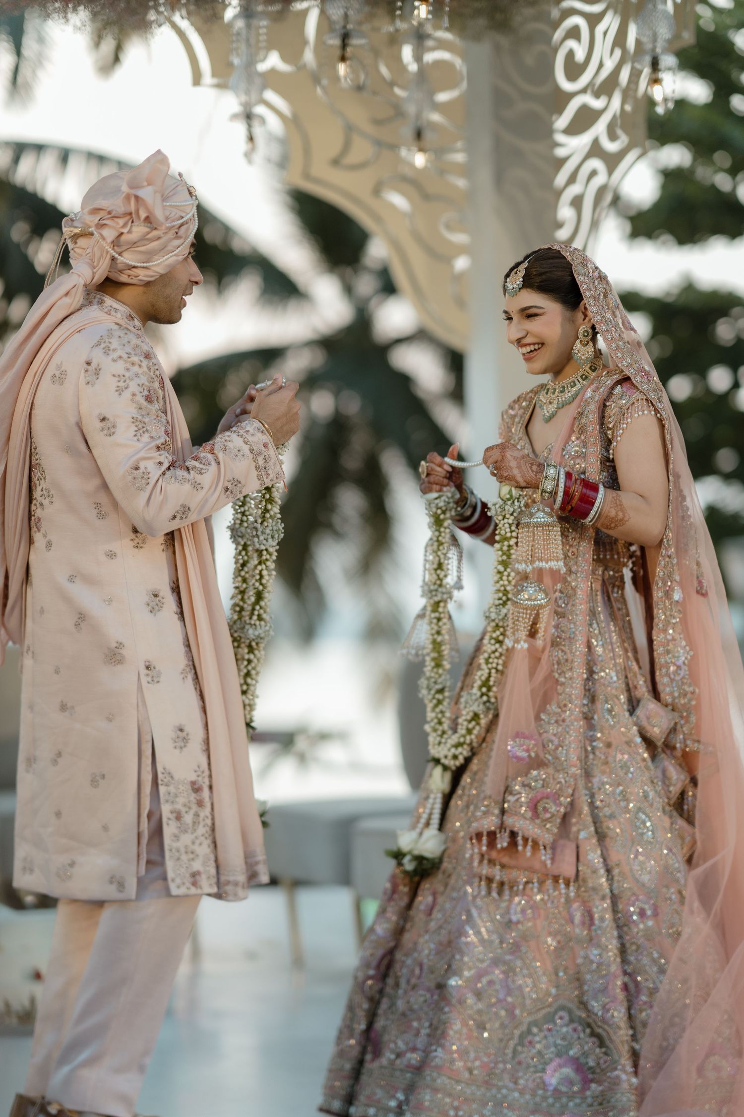 Romantic wedding scene with couple in matching blush pink and embellished traditional Indian attire.