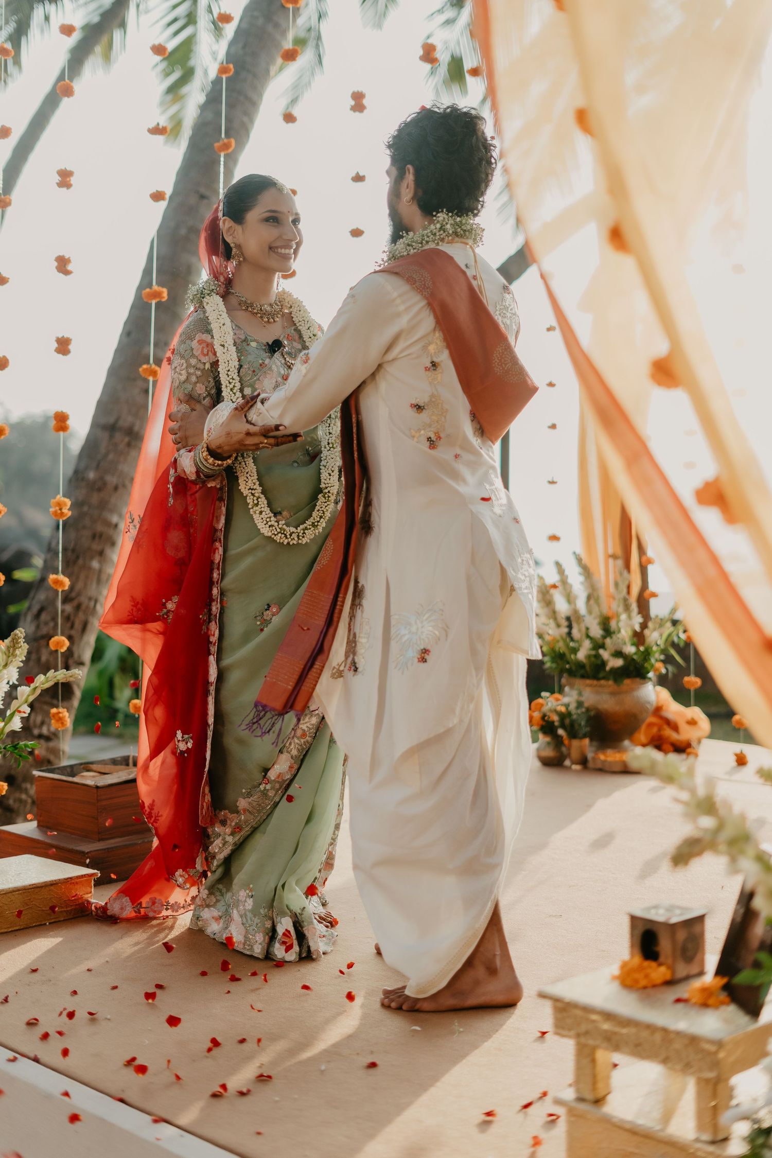 Indian bride in green saree and groom in white kurta exchange garlands at a traditional Hindu wedding ceremony.