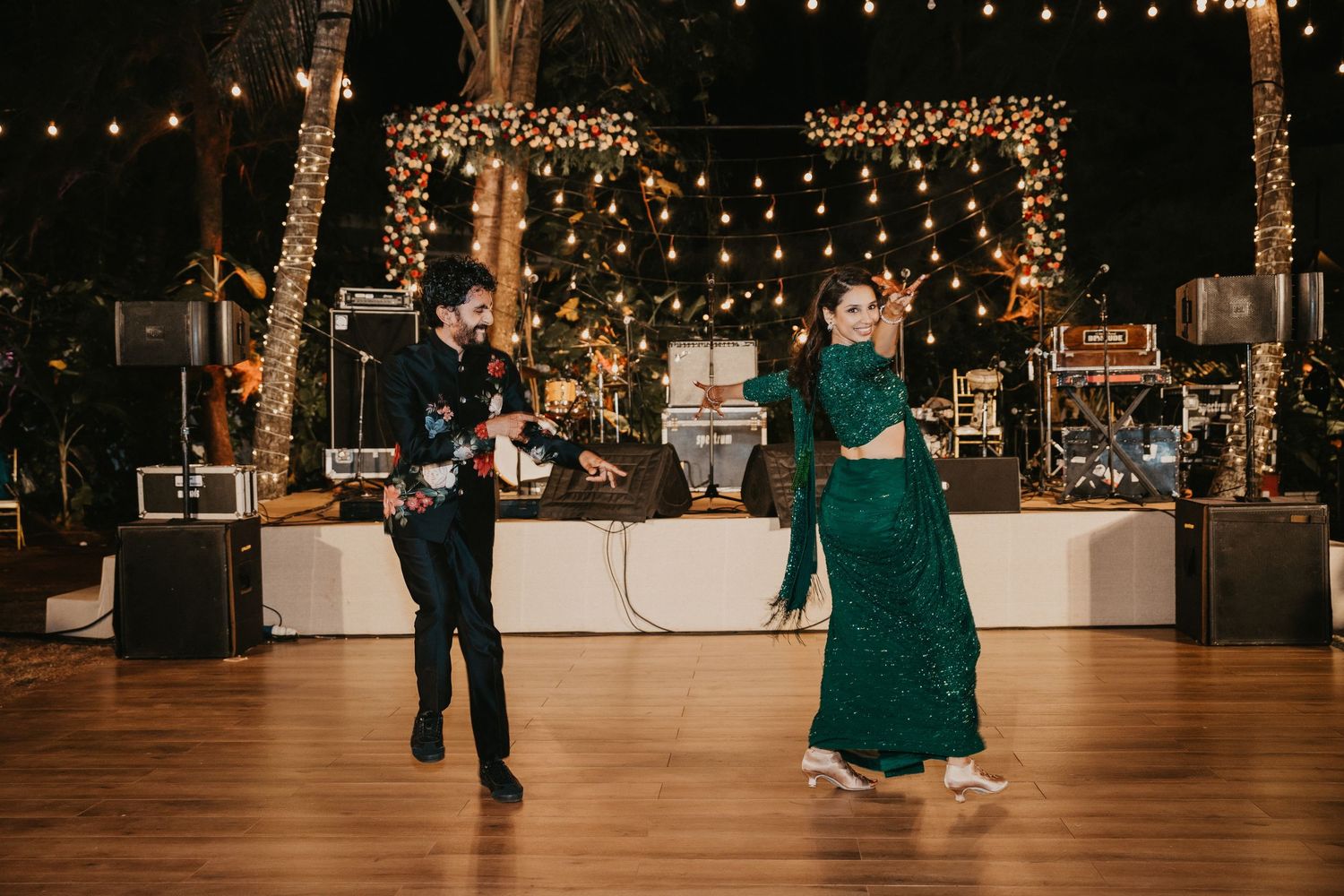 Couple dancing at an elegant outdoor wedding reception with string lights and a live band in the background.