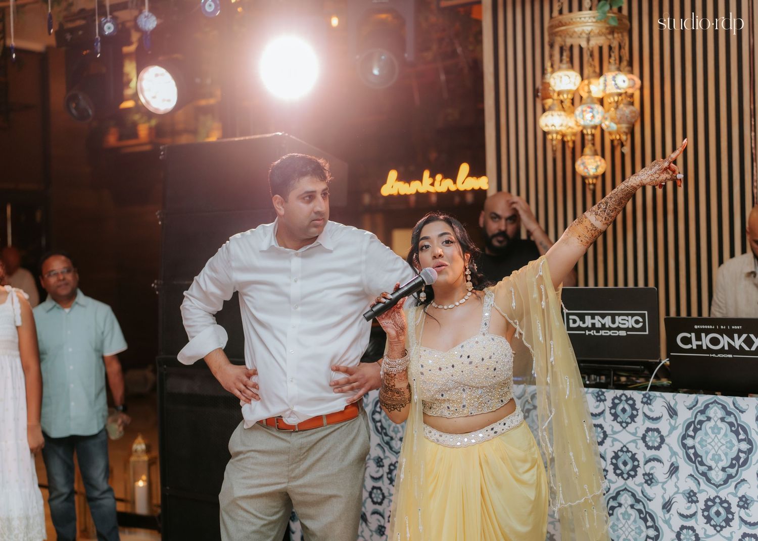 Couple dancing joyfully at an Indian wedding celebration in a festive venue with colorful lights.