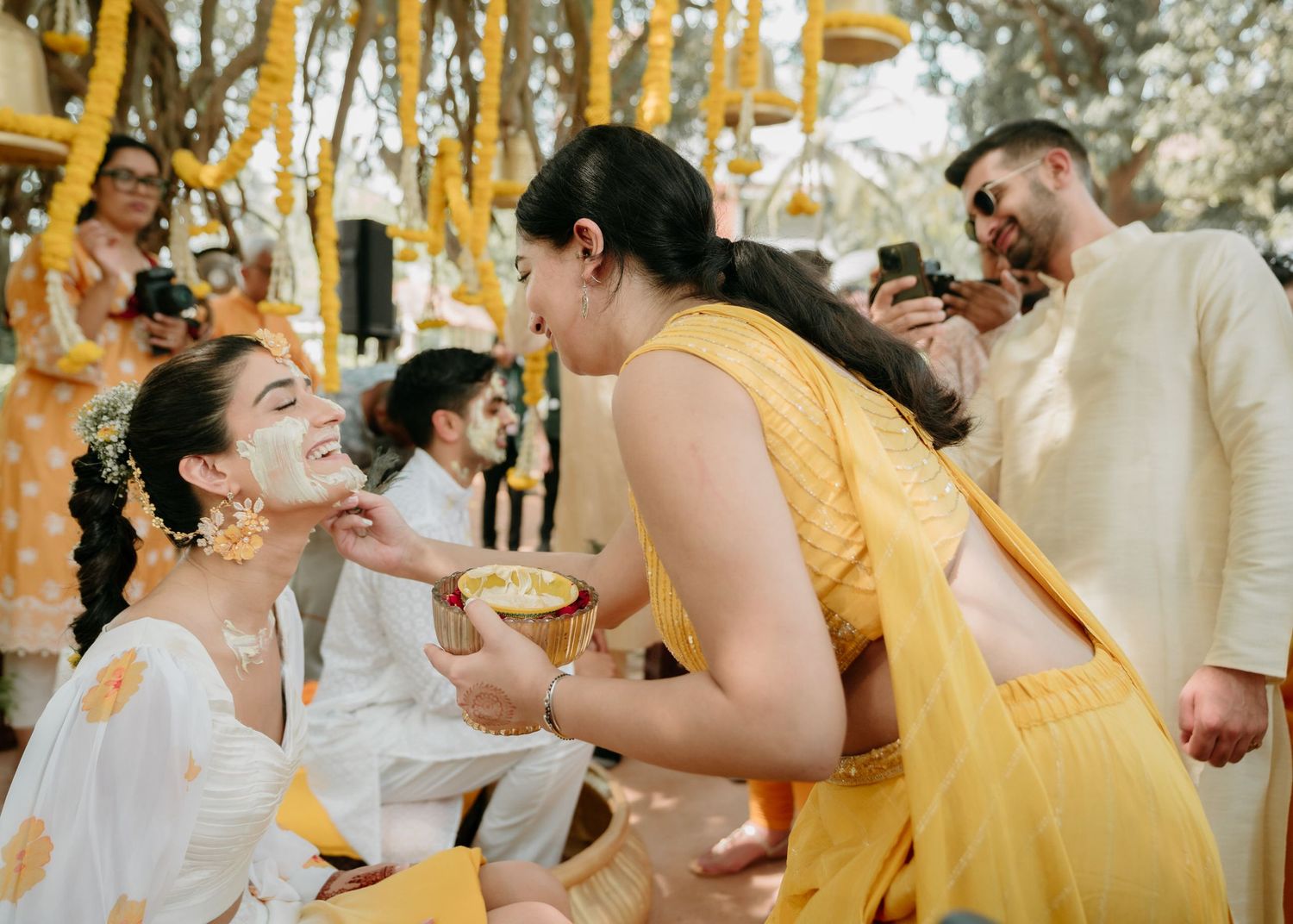 A series of candid moments at a wedding celebration with people in yellow and white attire sharing toasts and laughter.