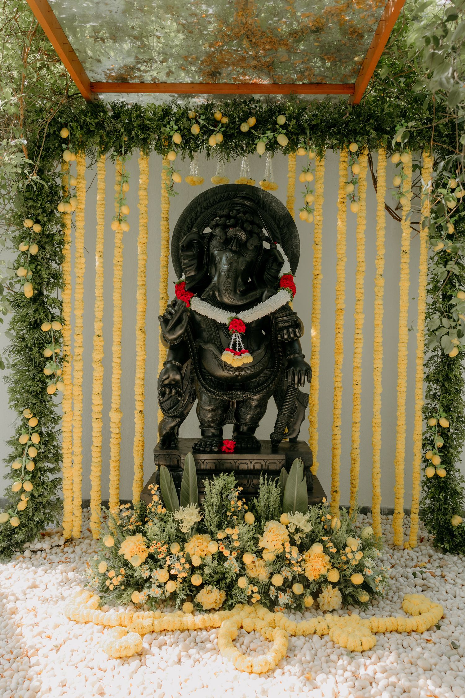 A decorated Ganesha idol adorned with flowers and yellow marigold garlands against a striped backdrop in a temple setting.