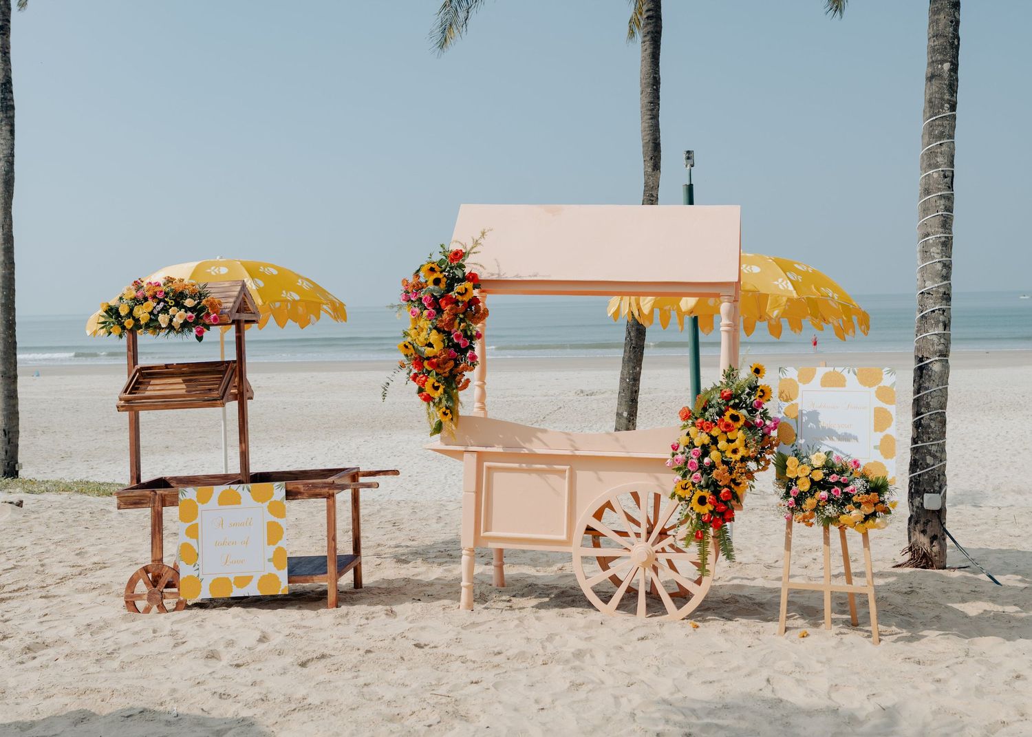 Rustic pink and white beach wedding arch with floral arrangements and palm trees in the background creates a romantic setting.
