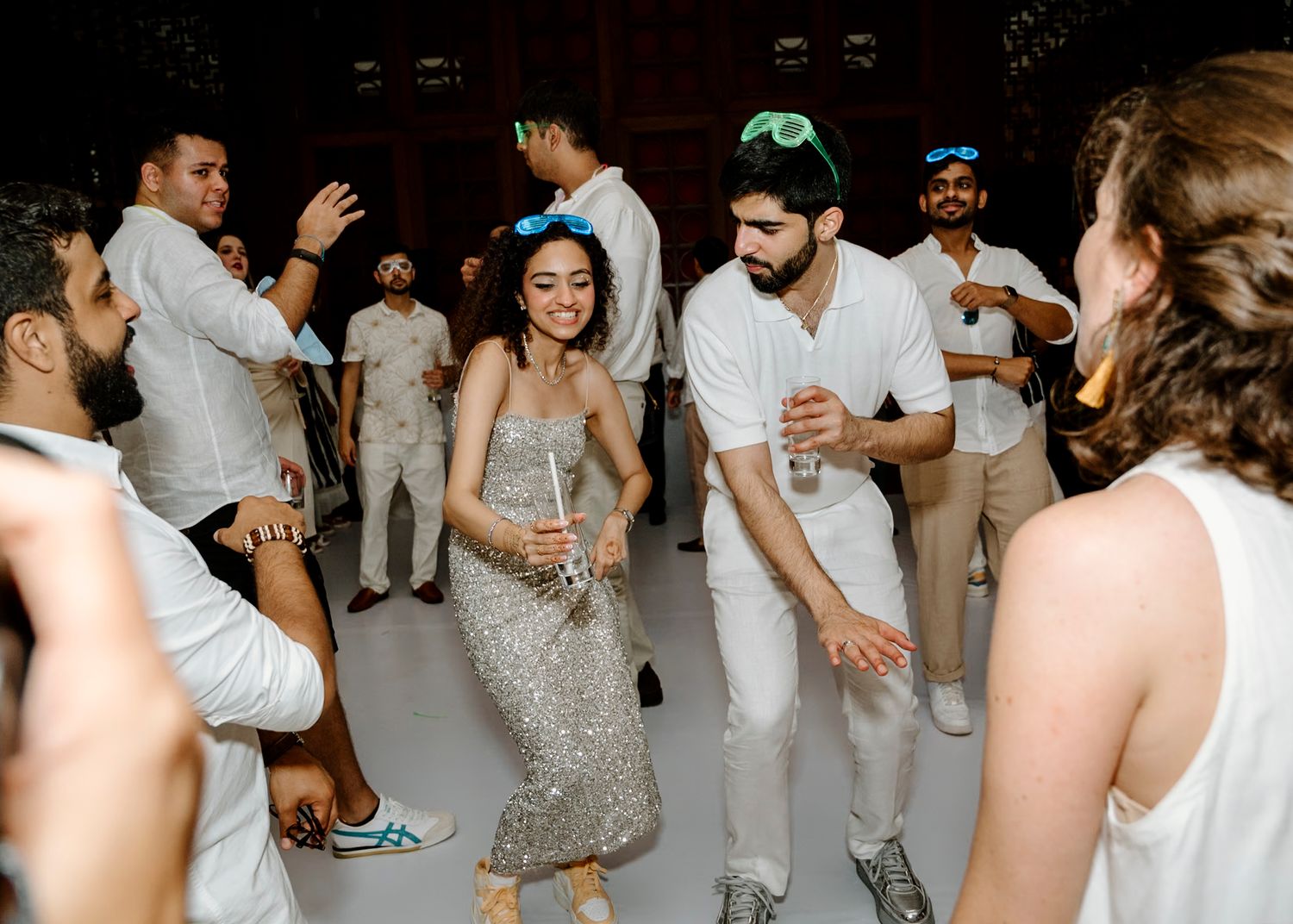 Wedding guests dance in white attire during a lively reception celebration.