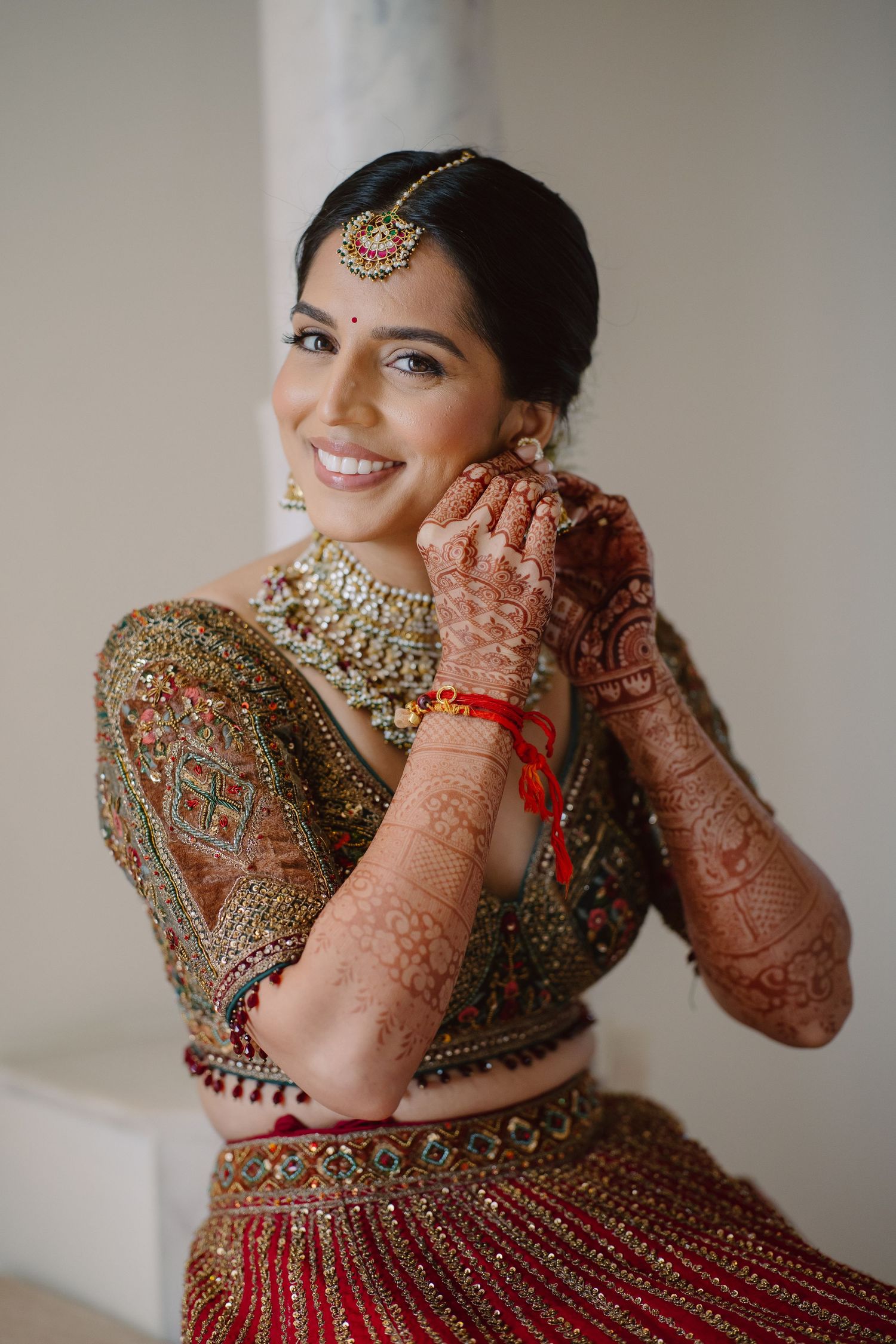 Traditional Indian bride wearing red lehenga with ornate jewelry and henna decorated hands.