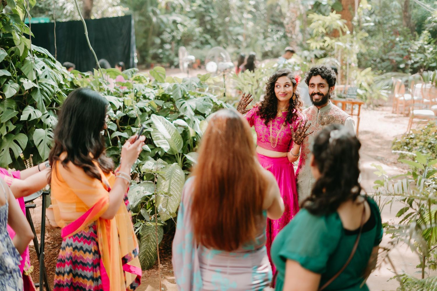 Guests in colorful traditional attire gather outdoors among lush greenery at a vibrant Indian celebration.