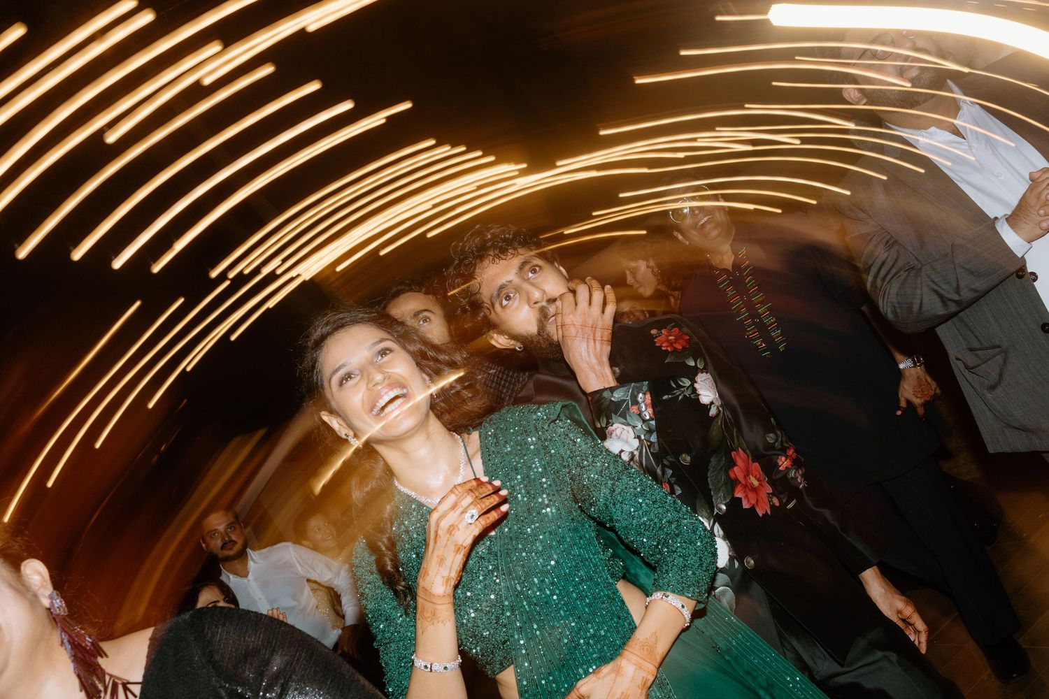 People dancing joyfully at a party with swirling light trails in the background, woman in green dress laughing.