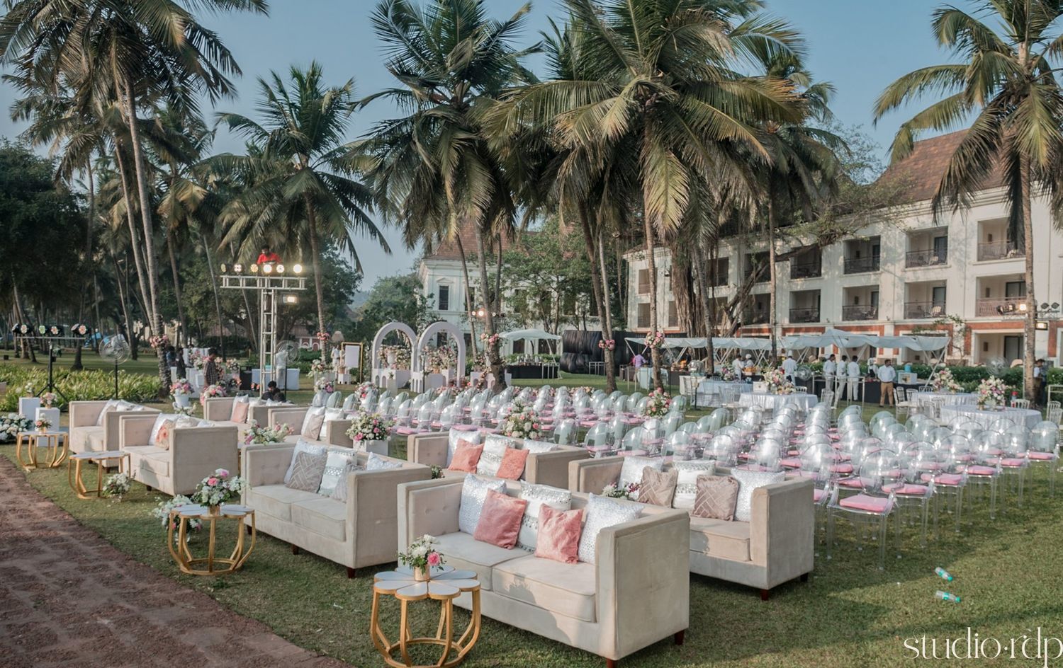 Luxurious outdoor beach wedding setup with white lounge seating and palm trees in a tropical setting.