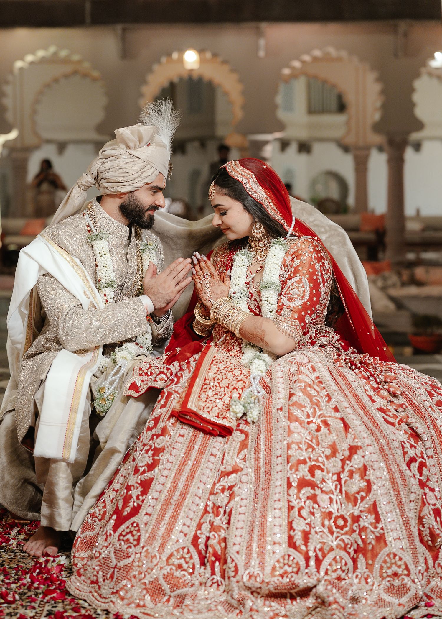 Indian bride and groom in ornate red and gold wedding attire sharing an intimate moment.