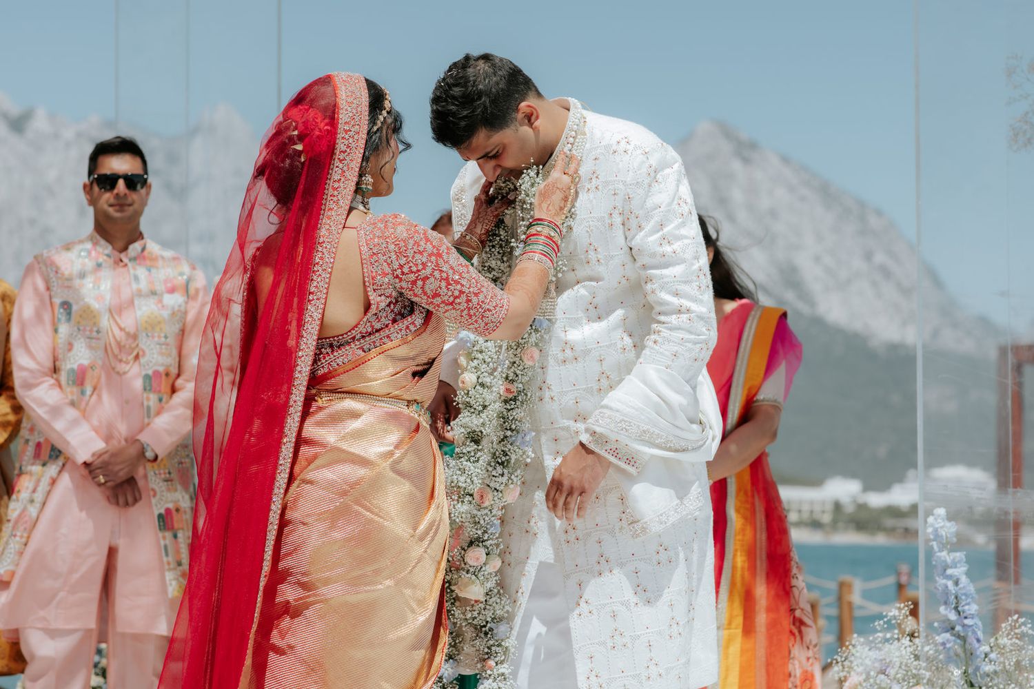 Indian bride and groom exchange garlands during traditional Hindu wedding ceremony with mountain backdrop.