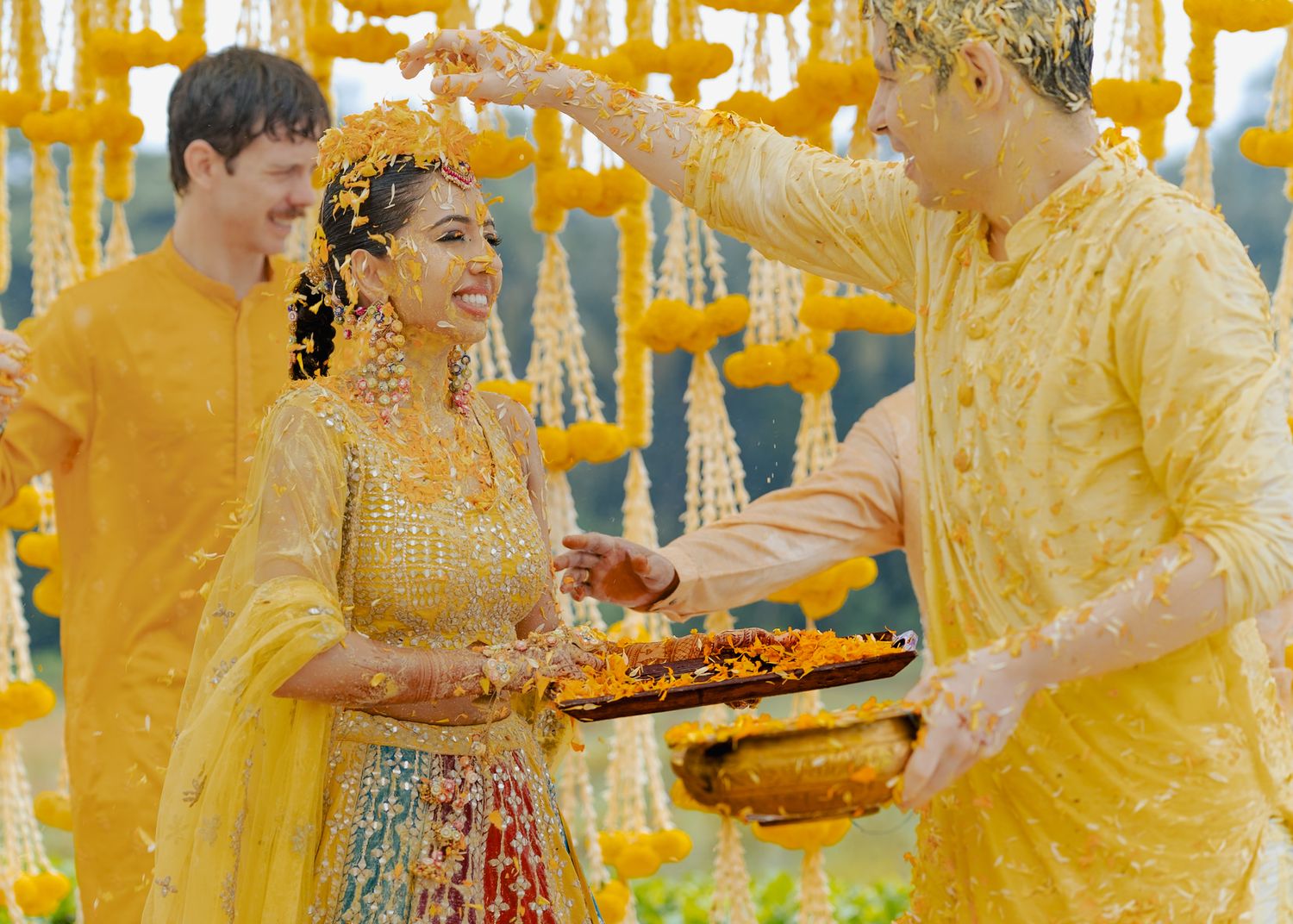 Guests in yellow outfits celebrate during a traditional Haldi ceremony with turmeric powder.
