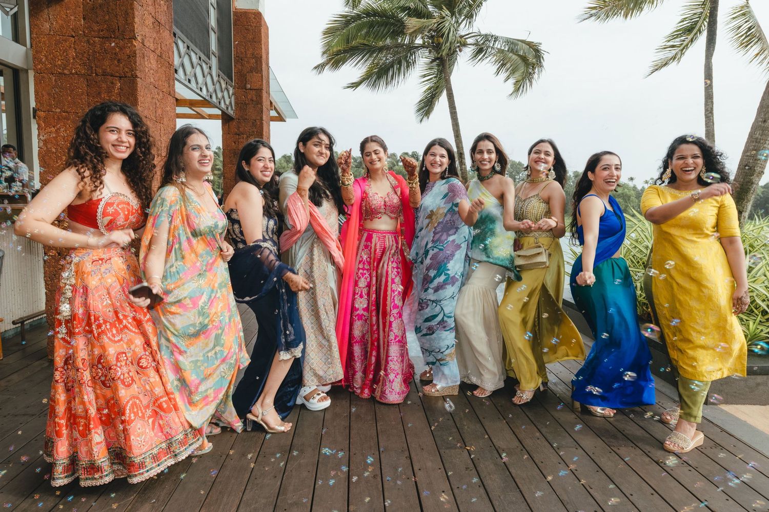 Group of women in vibrant Indian traditional attire posing outdoors at a tropical wedding celebration.